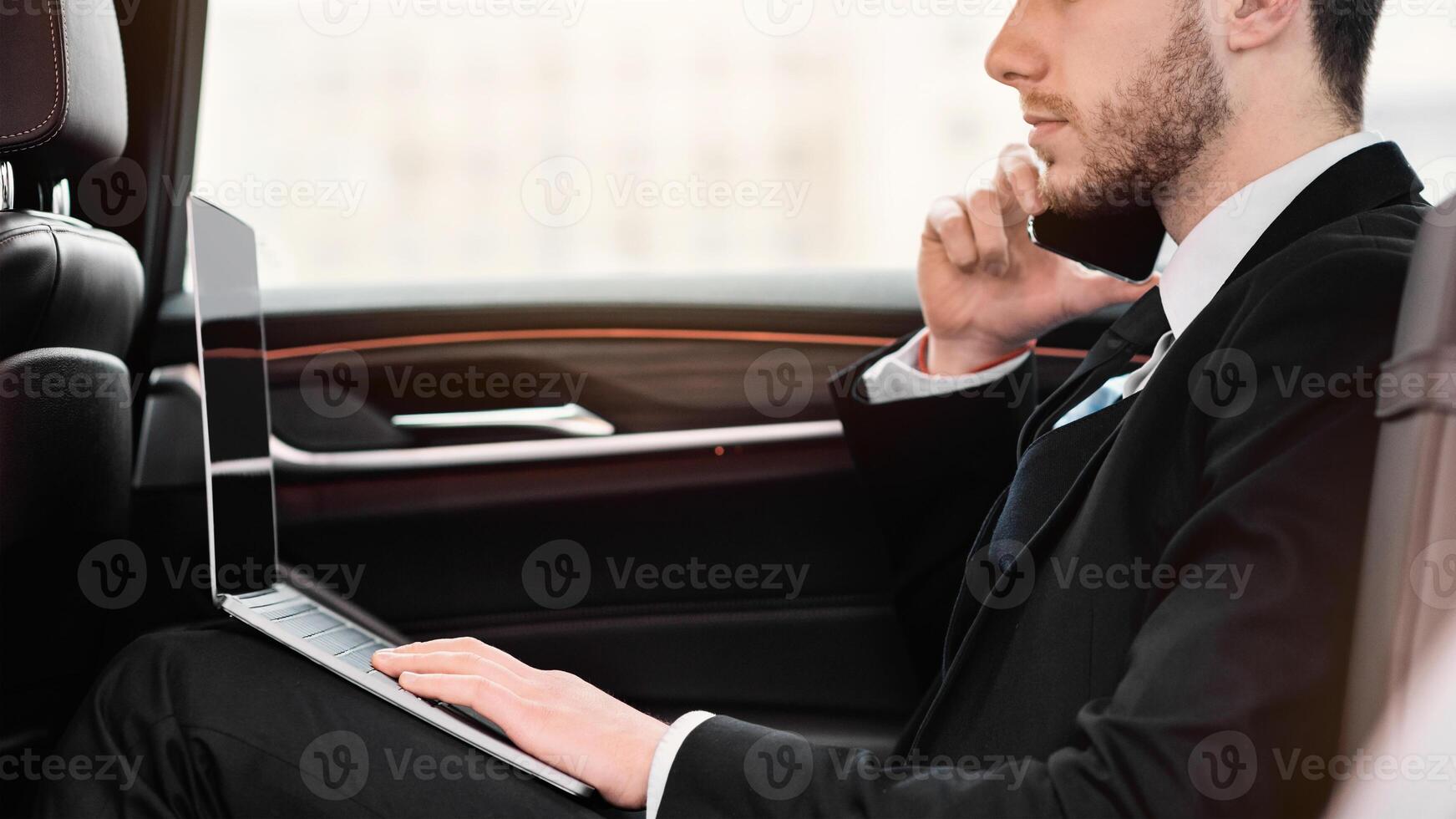 Always In Touch. Confident chief executive in suit using personal computer and making phone call in taxi, copy space, side view photo