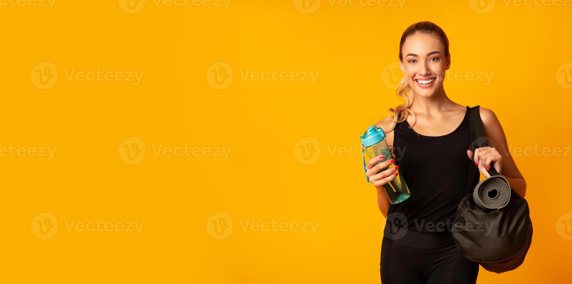 Woman Holding Fitness Bag, Rolling Mat And Water Ready For Training. Yellow Background, Studio Shot, Panorama With Free Space photo