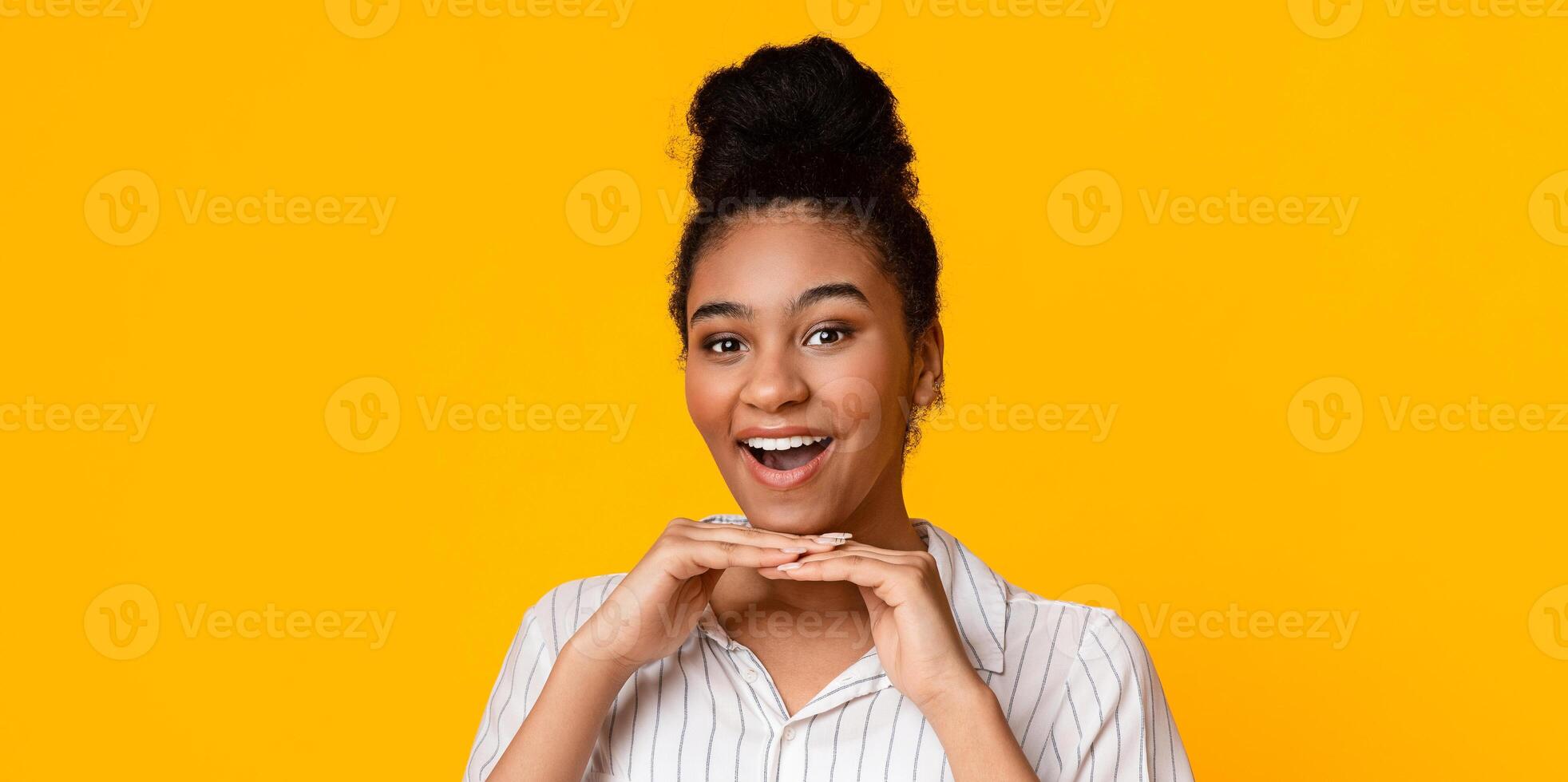 Joyful Black Girl Leaning Chin On Hands And Smiling At Camera, Posing On Yellow Studio Background With Empty Space photo