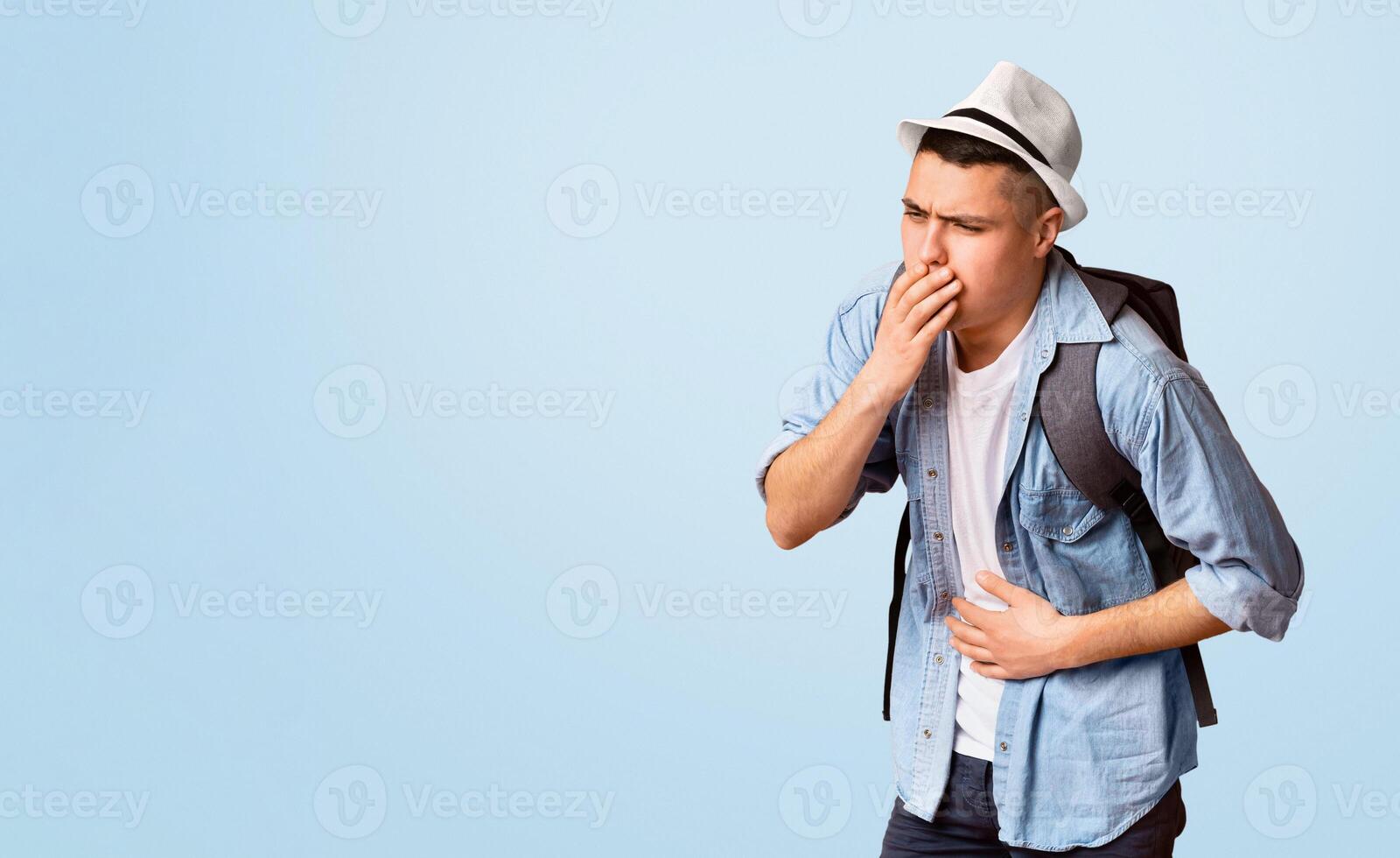 Young guy traveler having problems with digestive, holding belly and touching moth over orange studio background photo