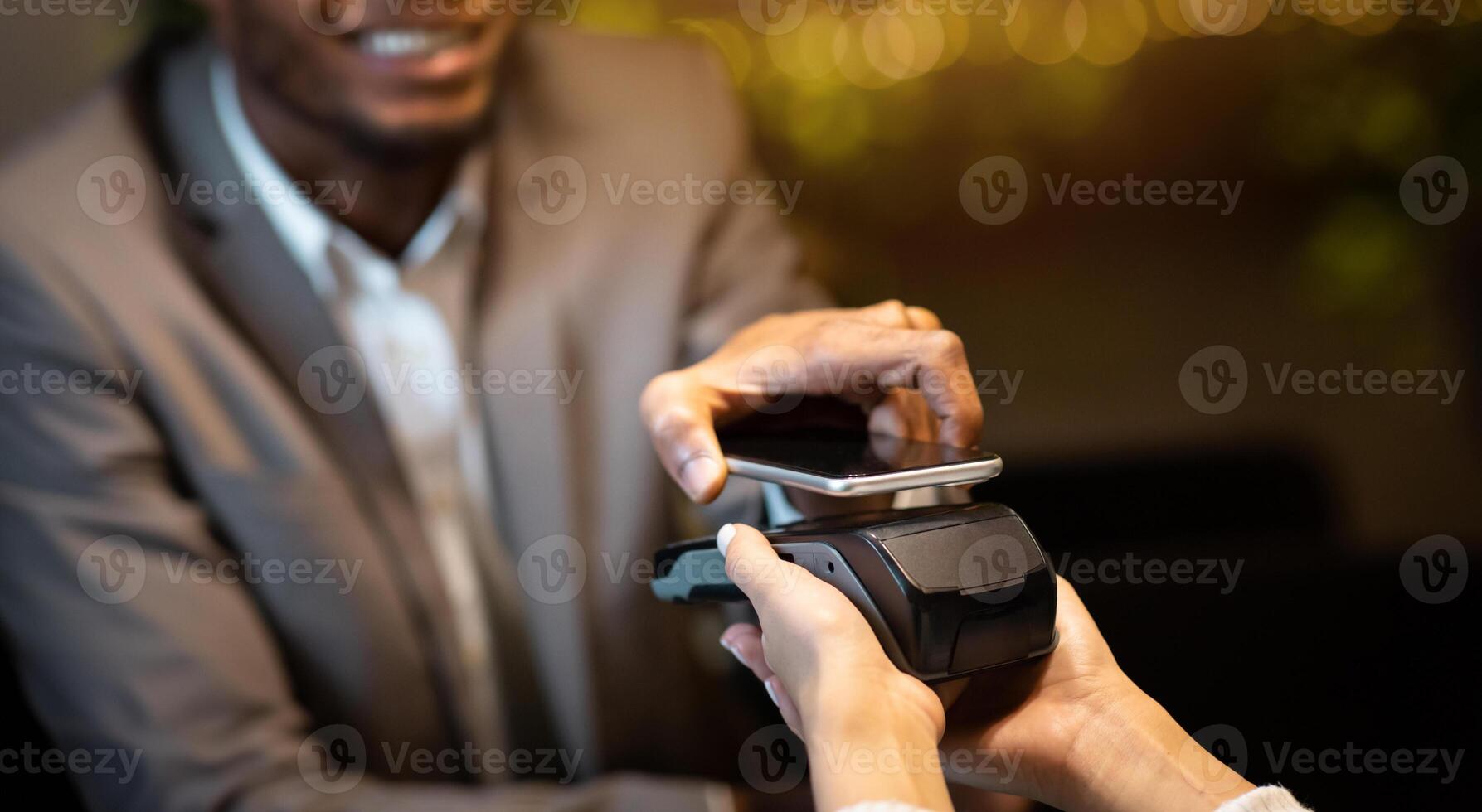 Contactless Payment System. Happy black businessman holding cellphone close to electronic payment machine and paying photo
