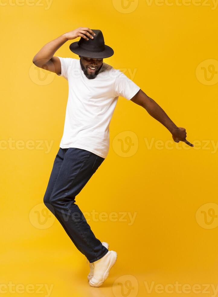 Cheerful african man dancing on tiptoes, copy michael jackson style on yellow studio background photo