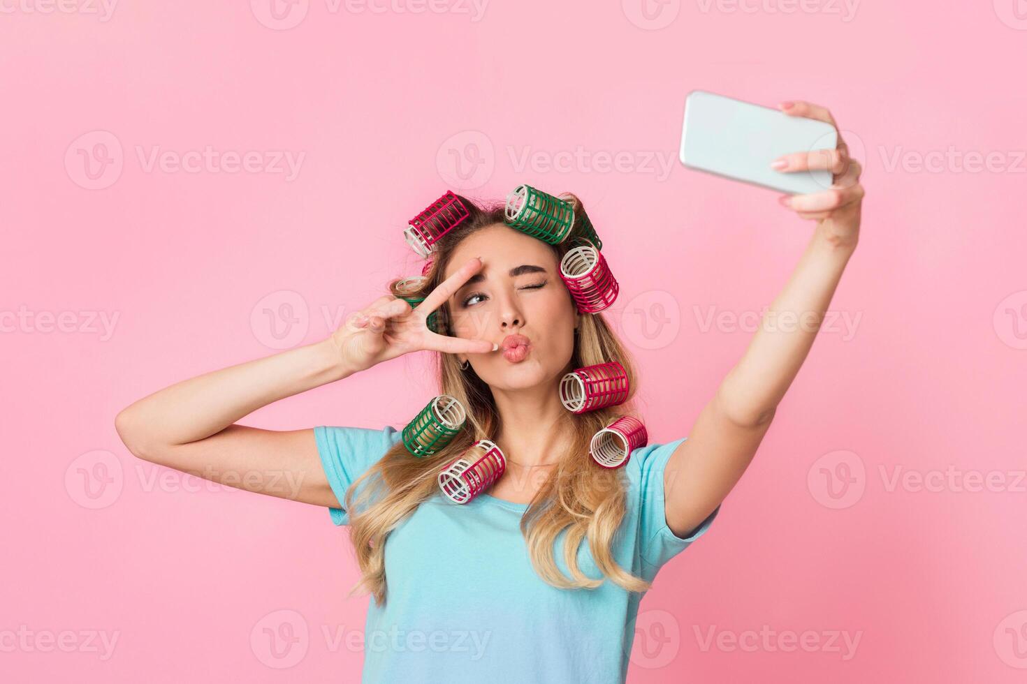 Social networks for housewife concept. Girl in curlers, make blowing kiss and winks, makes selfie photo