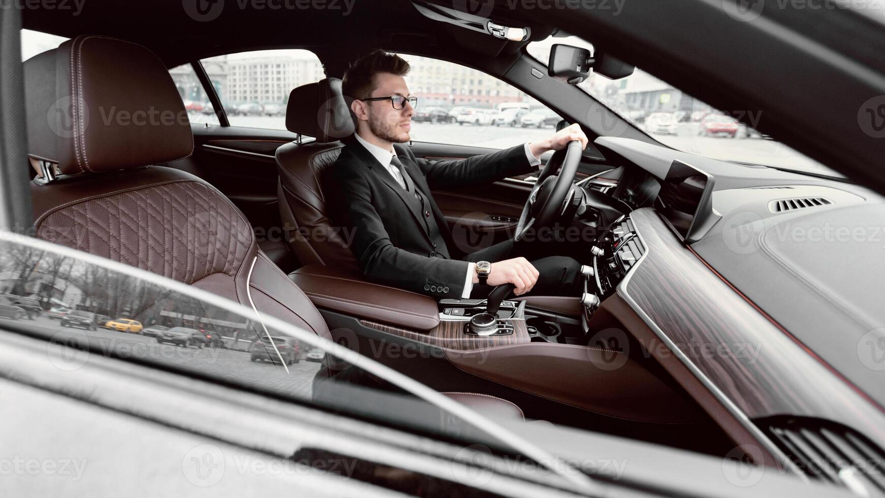 Attractive elegant business man wearing suit, glasses and wristwatch driving luxury car in urban city photo