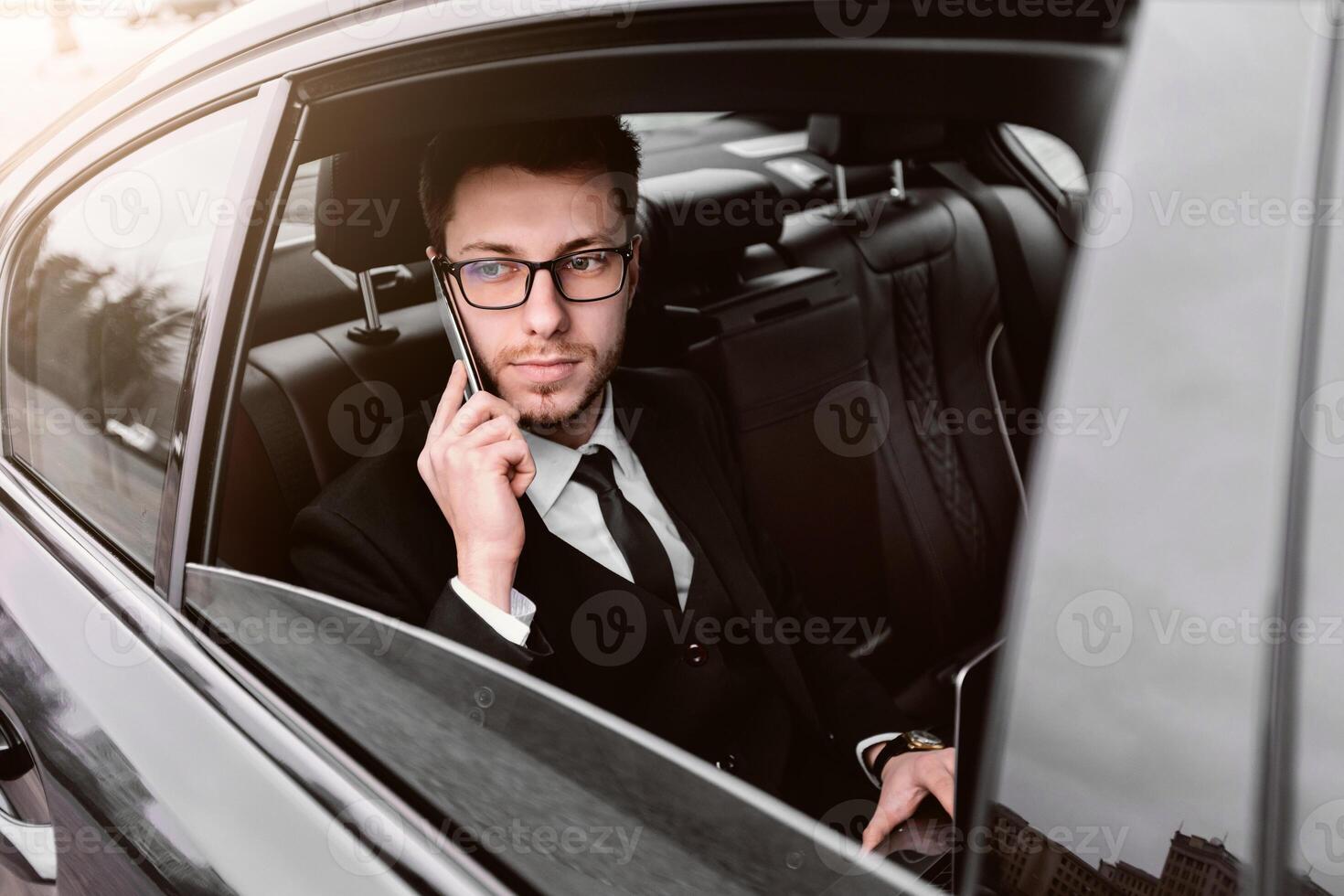 Always Available. Male ceo in suit and glasses talking on smart phone sitting in taxi cab, looking out of window photo