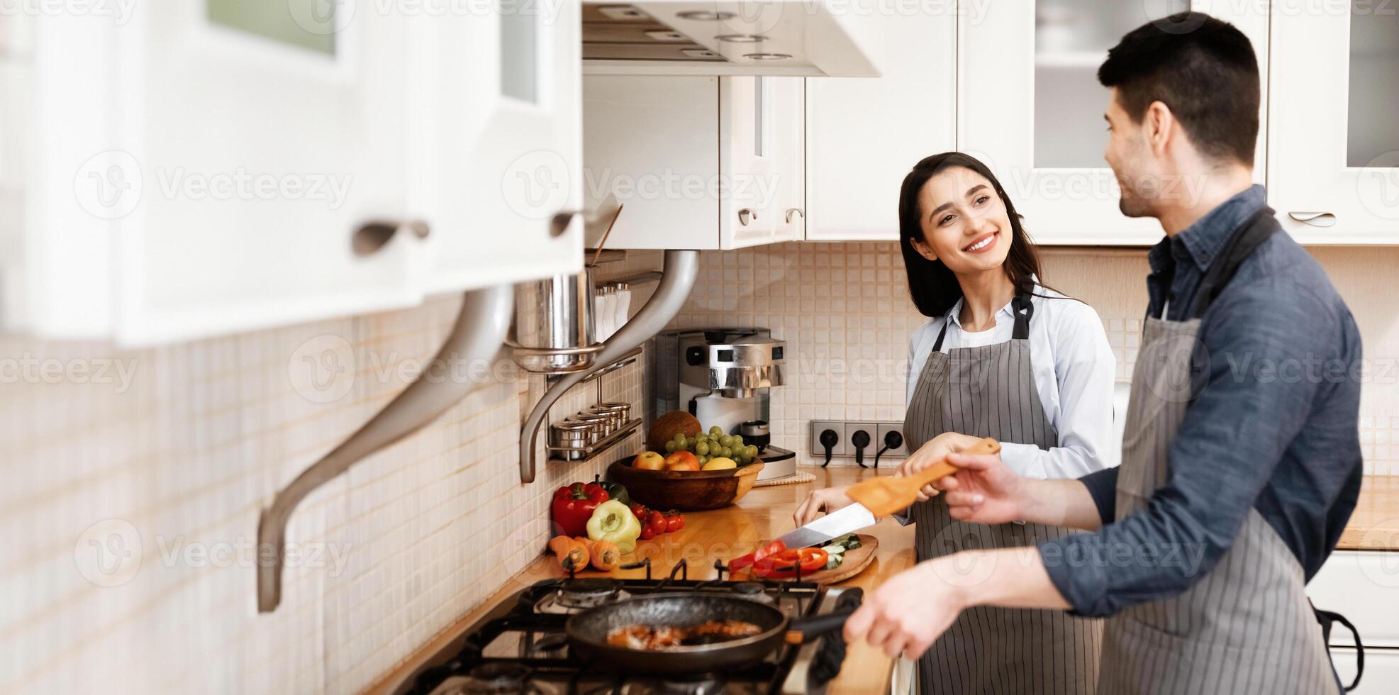 Cooking With Family. Happy couple preparing dinner together, frying and chopping vegetables, looking at each other photo