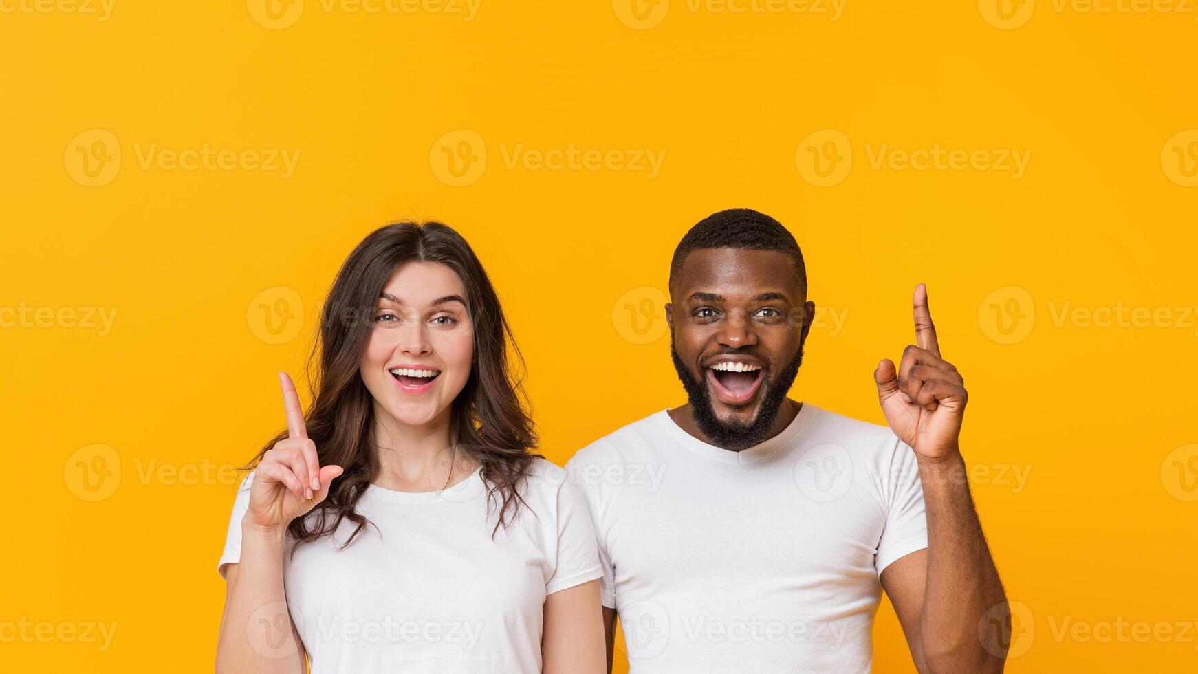 Couple Offer. Cheerful Afro Guy And Young Woman Having Idea, Foung Problem Solution, Pointing Fingers Up Over Yellow Background, Free Space photo
