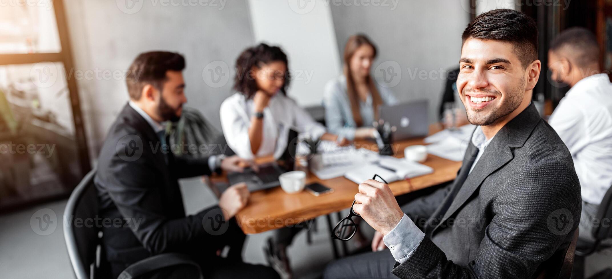 Corporate Meeting. Cheerful Businessman Smiling To Camera Sitting With Business Partners In Modern Office. Copy Space photo