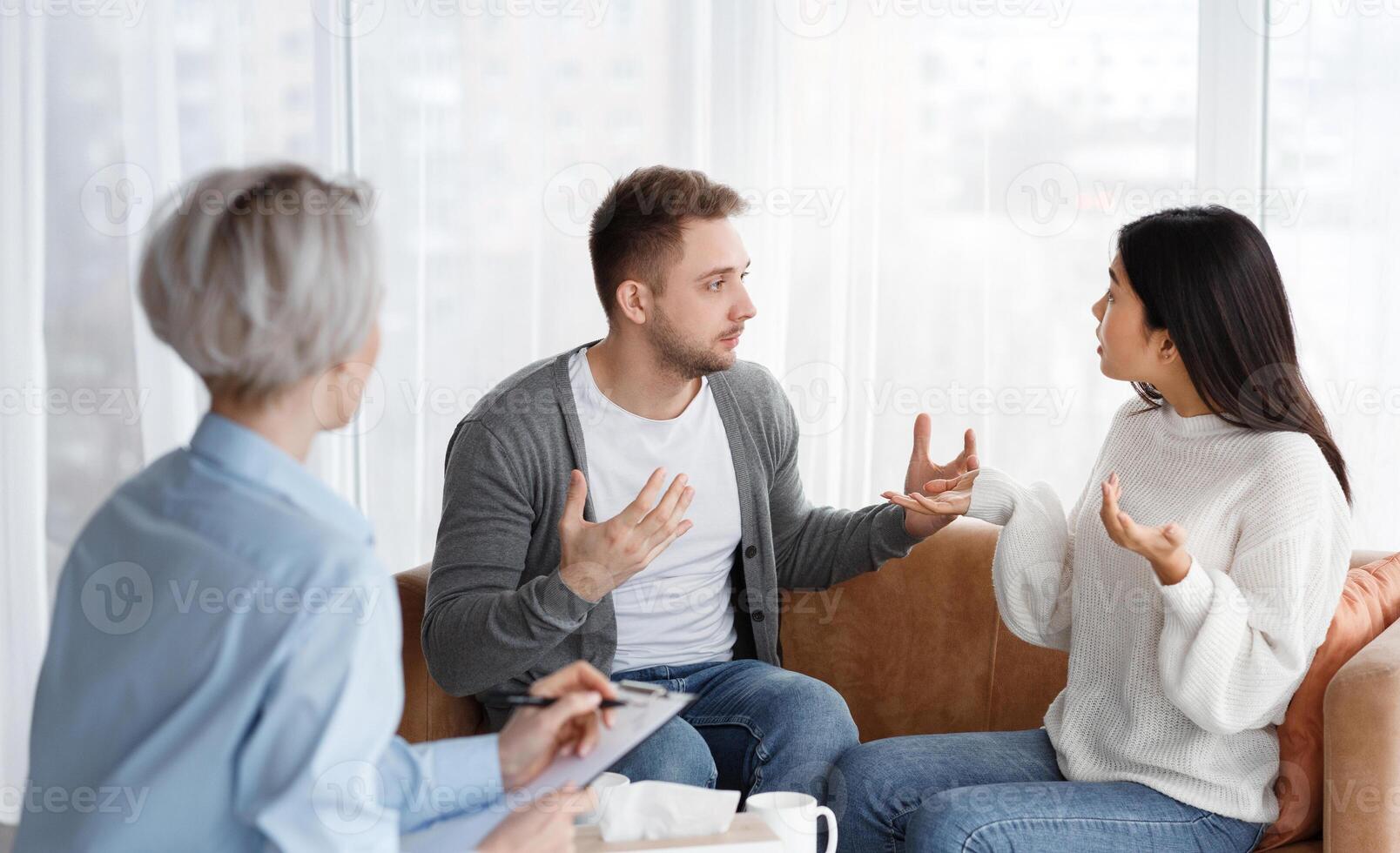 Family Conflicts. Married Couple Having Quarrel Blaming Each Other For Unhappy Life Sitting During Psychologist's Appointment In Office. Selective Focus photo