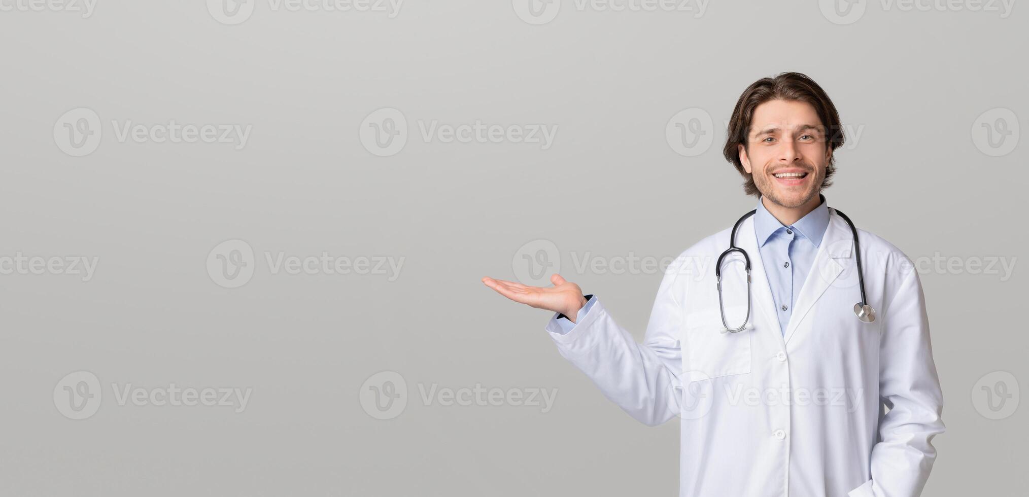Medical Offer. Smiling male physician pointing aside at copy space with his open palm, demonstrating new pill or treatment, panorama photo