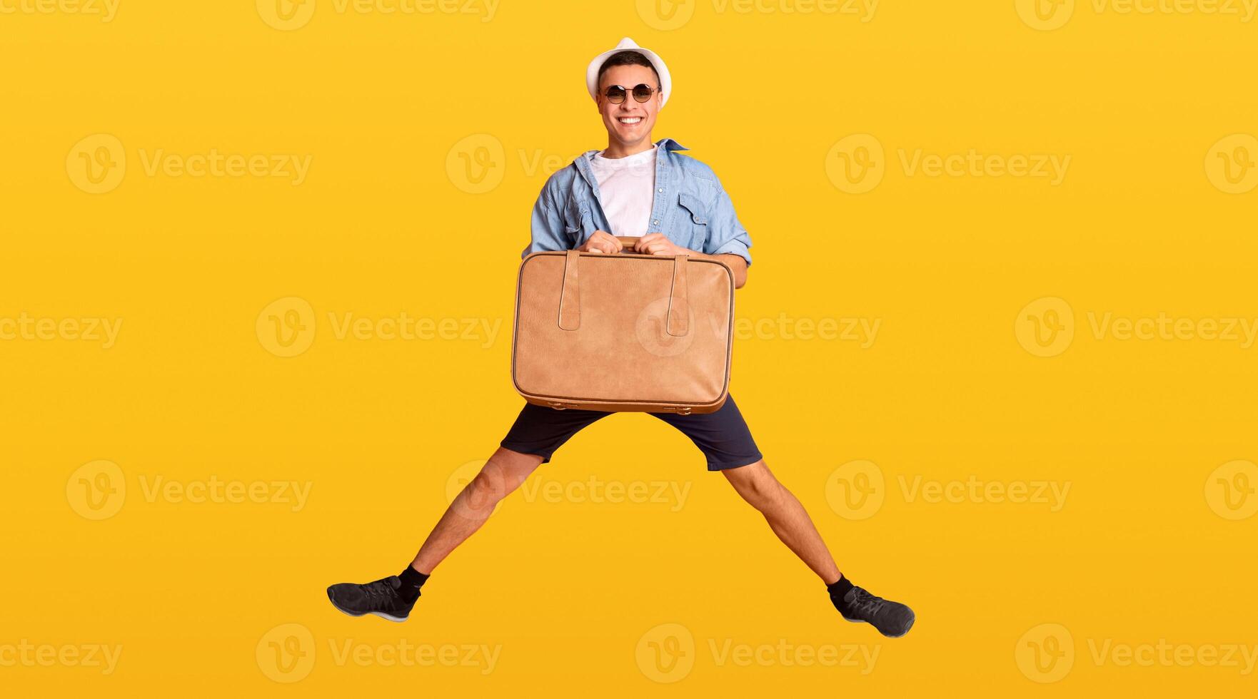 Happy guy tourist jumping with suitcase over orange background, panorama photo