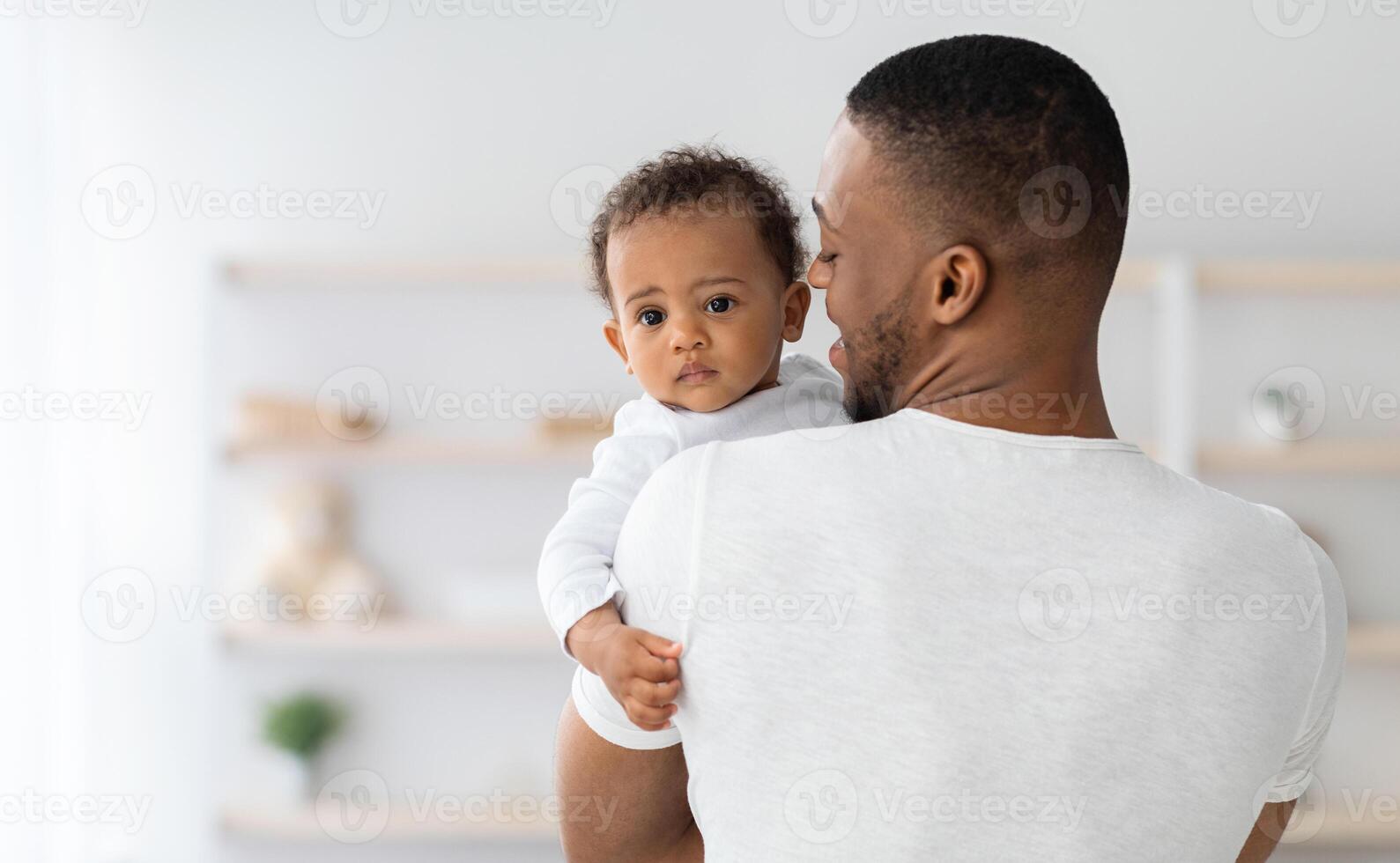 del padre amor. negro milenario hombre con adorable bebé chico en manos posando en hogar interior, amoroso africano americano papi participación su linda infantil niño, pequeño niño mirando a cámara, Copiar espacio foto