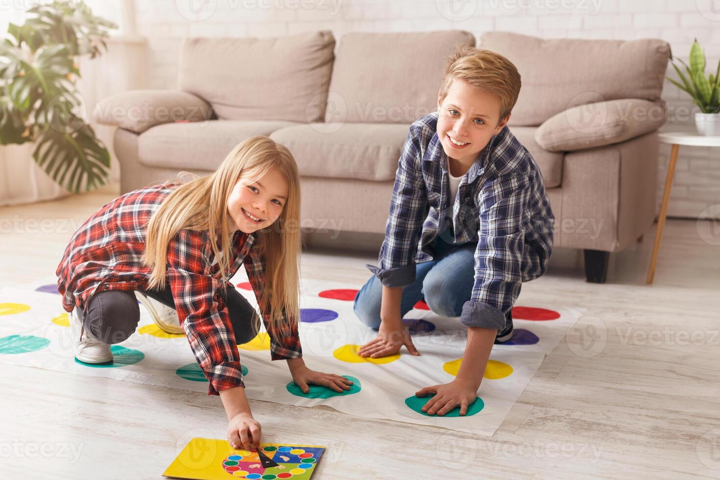 Cheerful siblings playing twister game on floor having fun at home on weekend. Kids friendship and leisure activities. photo