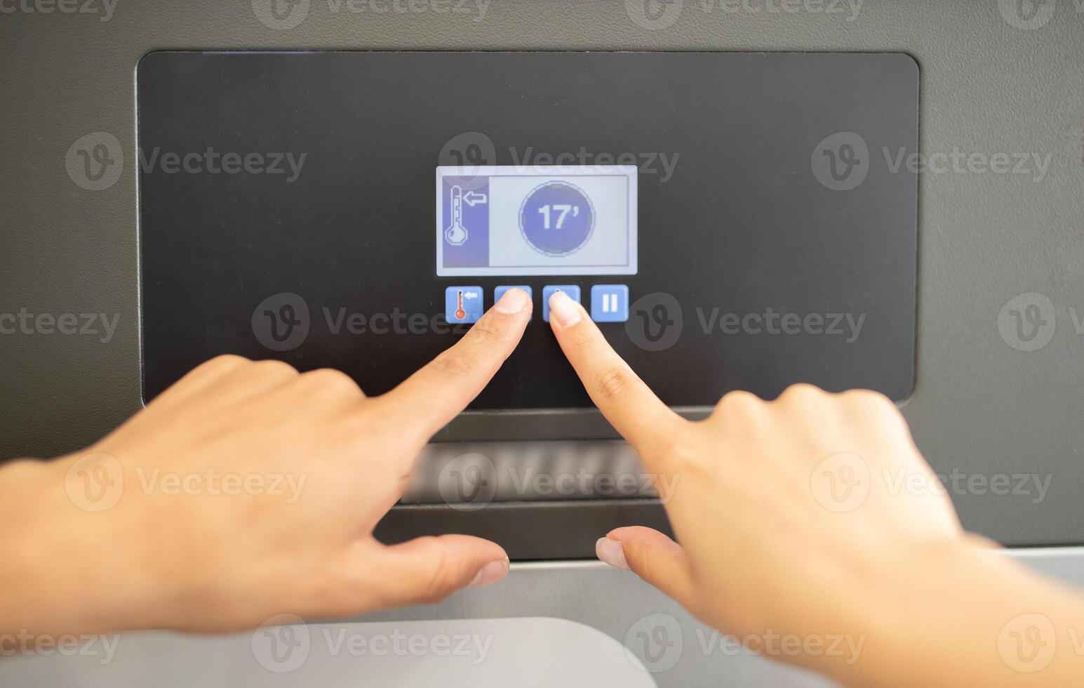 A person hands are seen adjusting the temperature settings on a sleek digital display panel in a kitchen. The display shows a temperature of 17 degrees, indicating precise control. photo
