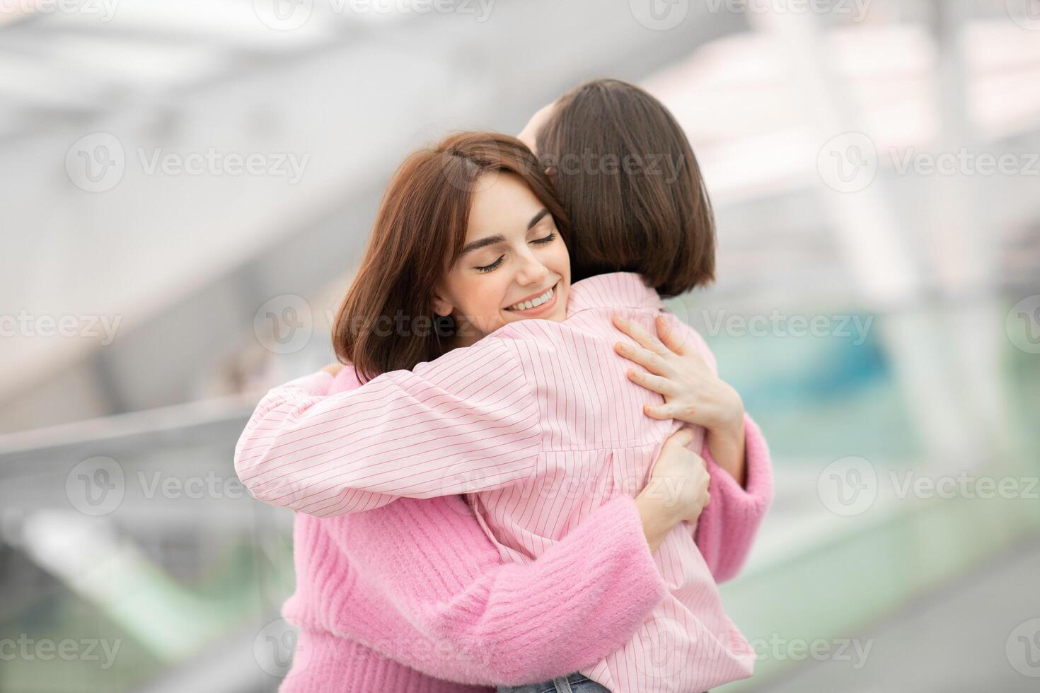 Two friends share a joyous hug in a contemporary environment, surrounded by soft natural light, showcasing a moment of friendship and connection. photo