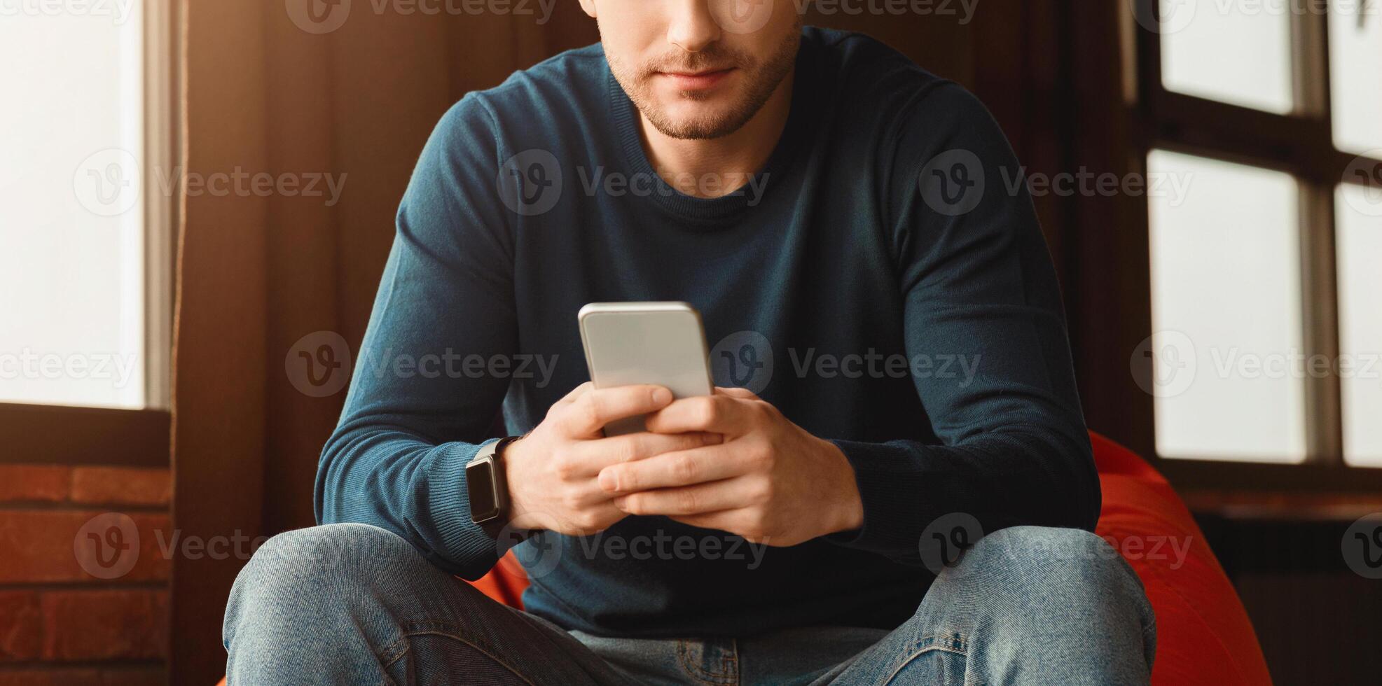 Unrecognizable Guy Using Mobile Phone Playing Games Sitting In Beanbag Chair Indoor. Panorama, Cropped, Selective Focus photo