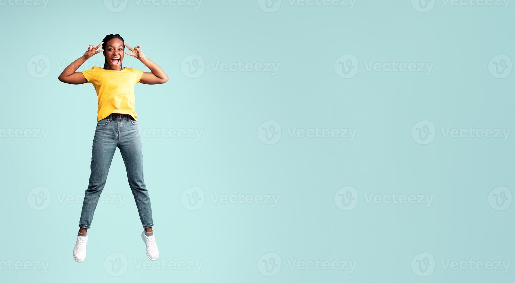 Joy Of Victory. Cheerful African American Lady Jumping Gesturing V-Sign Over Blue Studio Background. Full Length, Empty Space photo