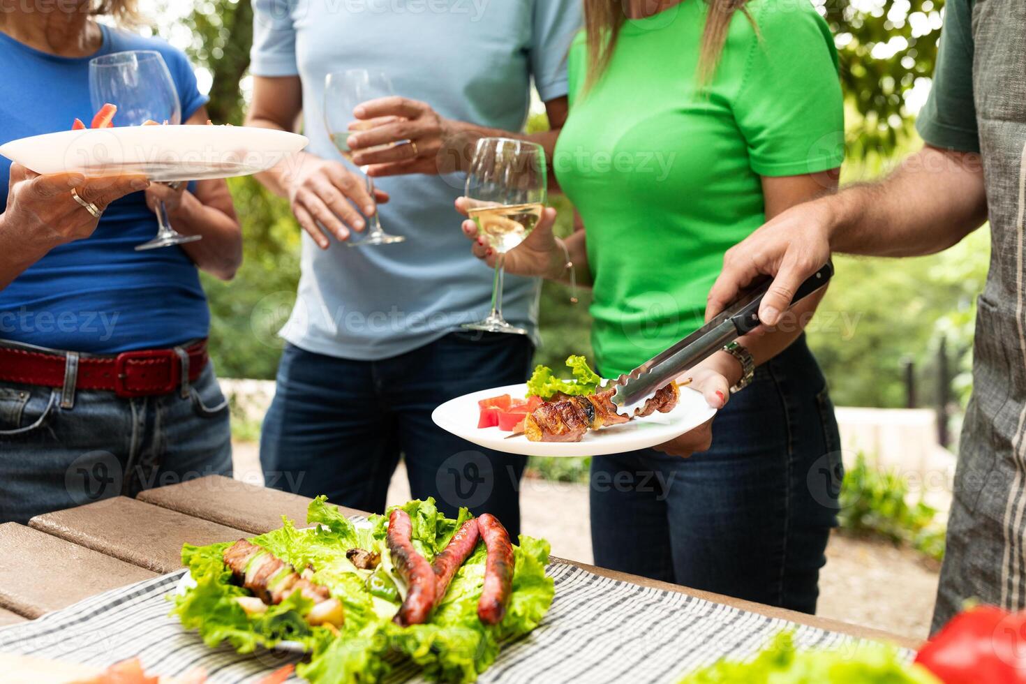 A group of friends gathers in a bright backyard to enjoy a summer barbecue. They serve salads and drinks while sharing laughter and good conversation under the sun. photo