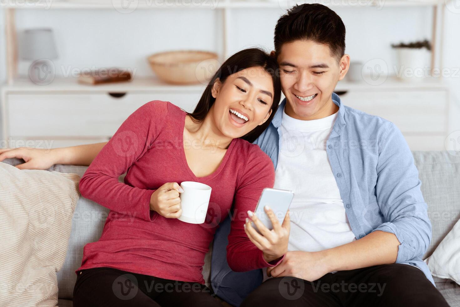 Family portrait of happy asian couple resting at home and watching on mobile phone together, empty space photo