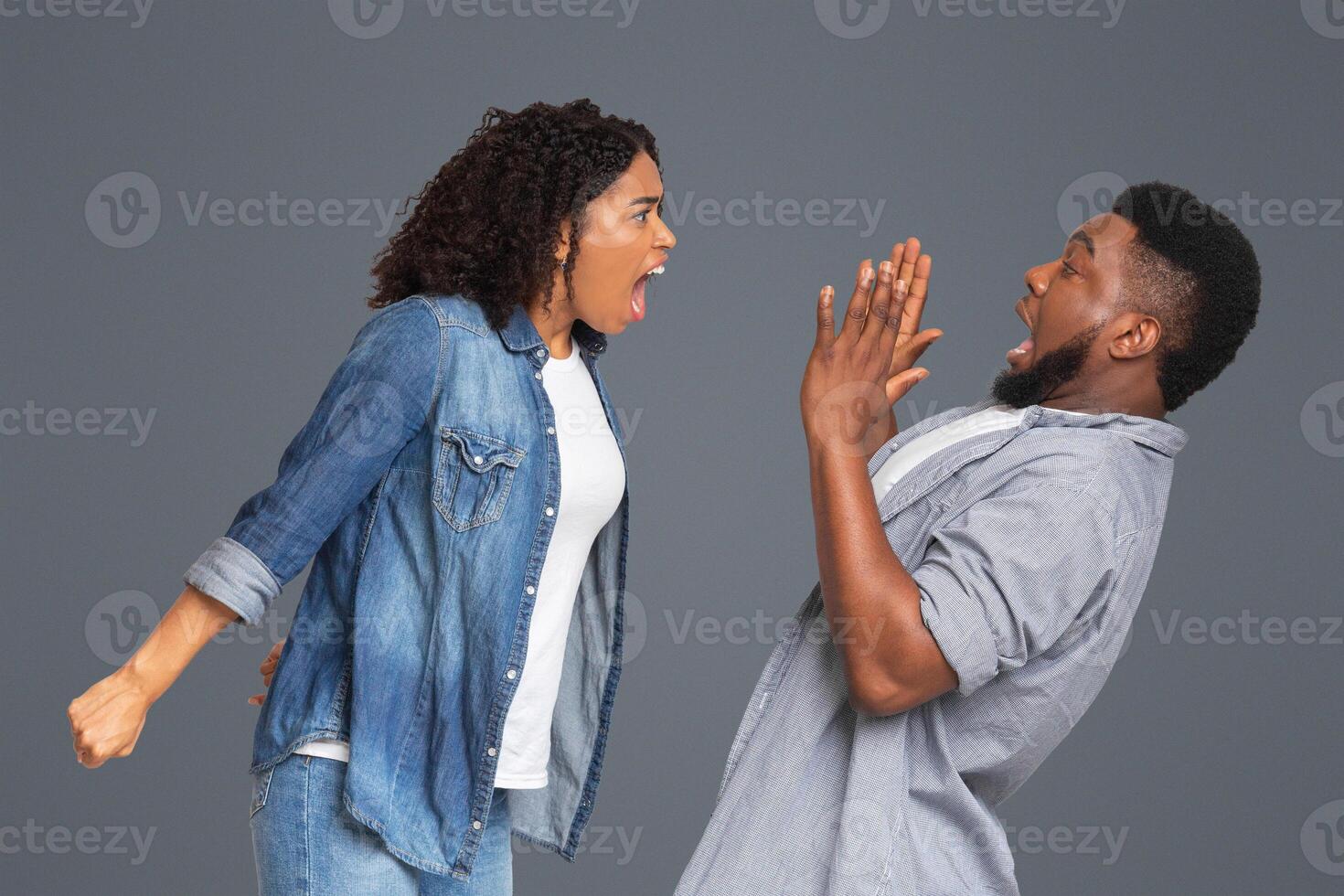 PMS Concept. Mad african american woman yelling at her scared boyfriend, shouting with rage on light studio background, empty space photo