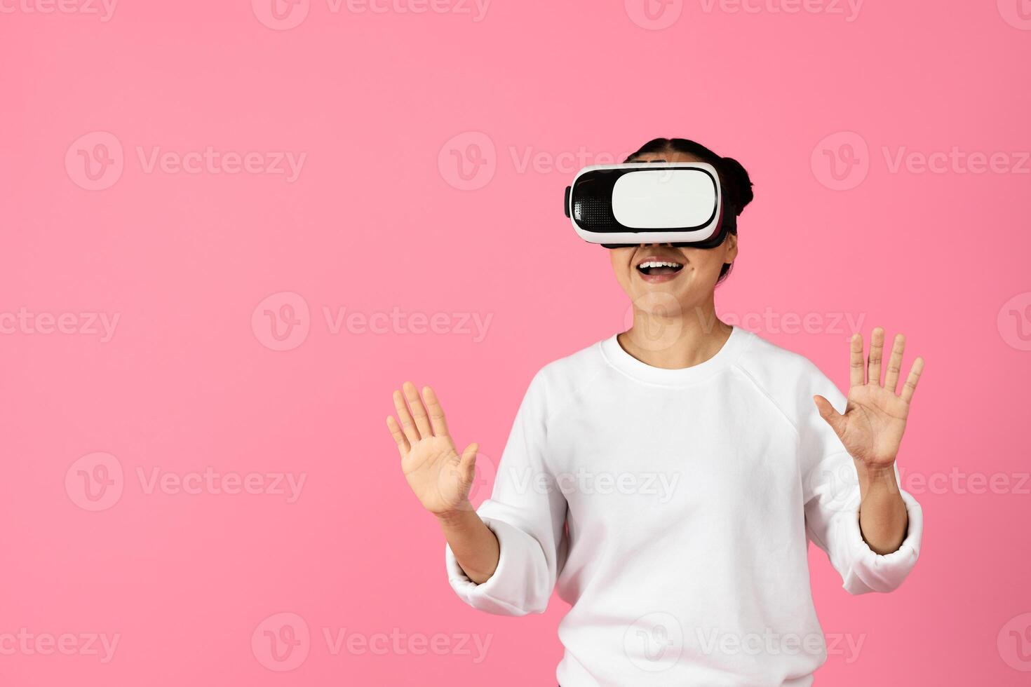 A woman is immersed in a virtual reality experience, wearing a headset and gesturing with her hands. Her expression conveys excitement and engagement as she explores a digital environment. photo