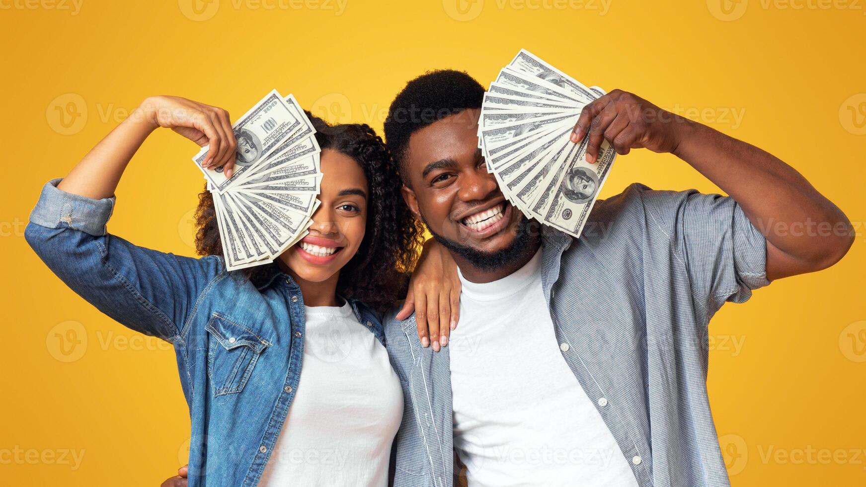 Lucky black man and woman holding lots of dollar cash, covering faces with money and cheerfully smiling photo