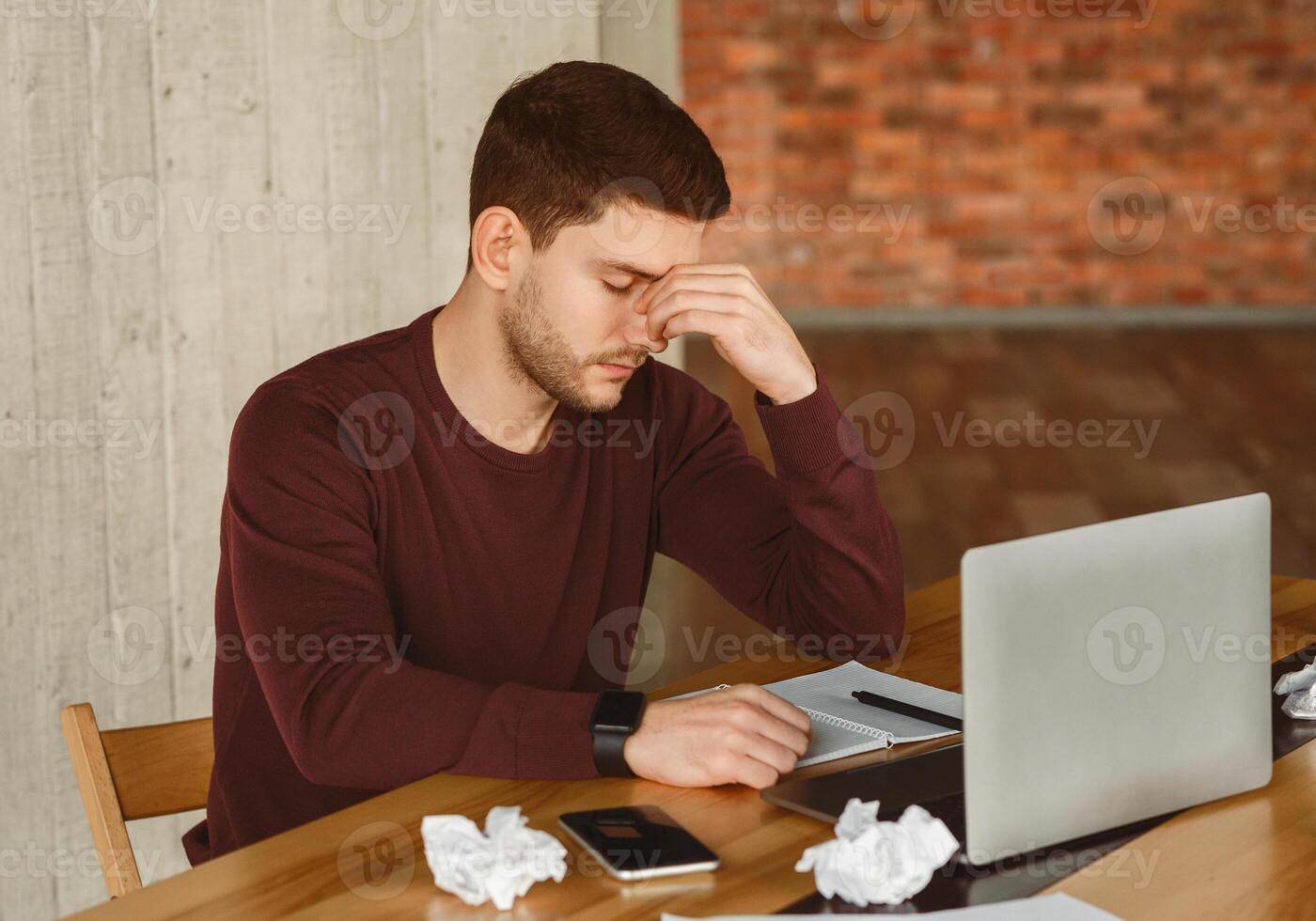 Tired Young Man Having Headache At Work, Touching Nosebridge Sitting At Laptop In Office photo