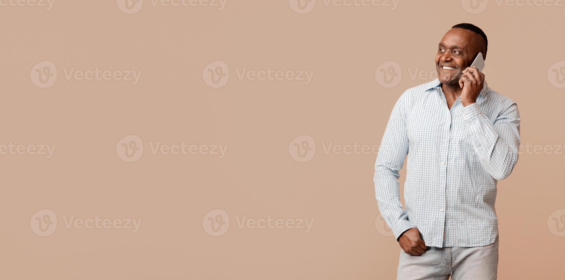 Modern communication. Positive mature afro man talking on cellphone, orange background with free space photo