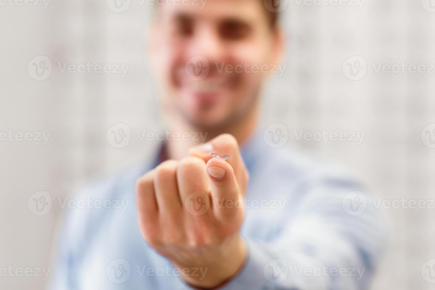 Smiling man holding and showing to camera contact eye lens on finger, copy space, selective focus photo