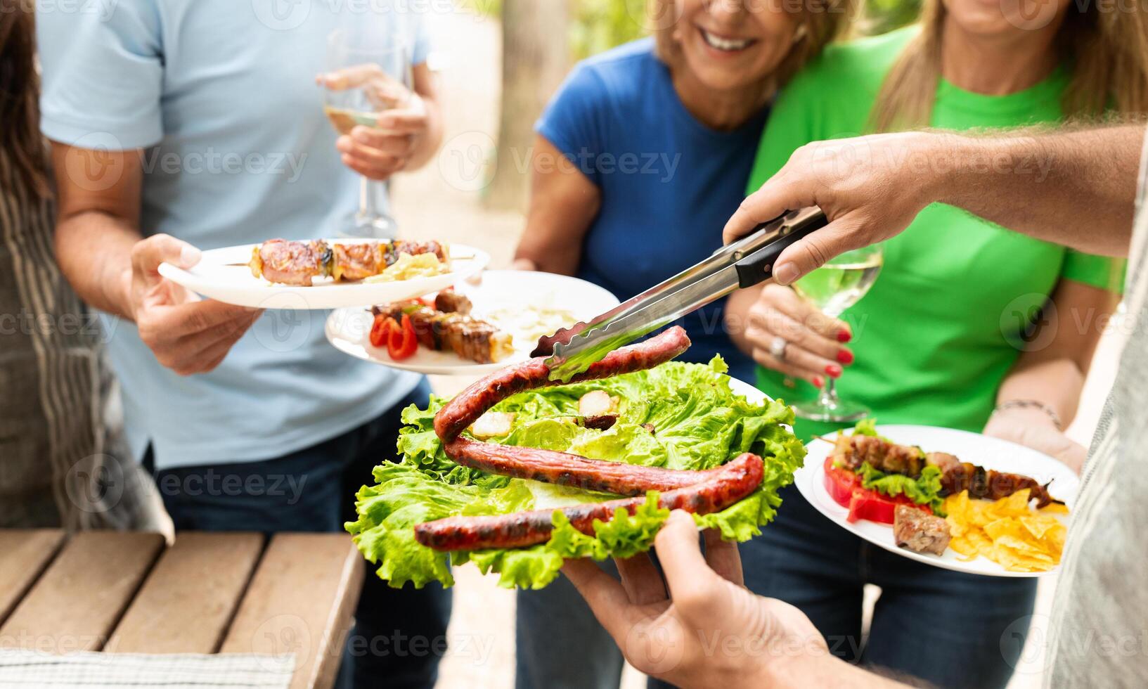 Group of friends gather outdoors for a barbecue, sharing delicious grilled sausages and fresh salads while enjoying drinks and each other's company on a sunny day. photo