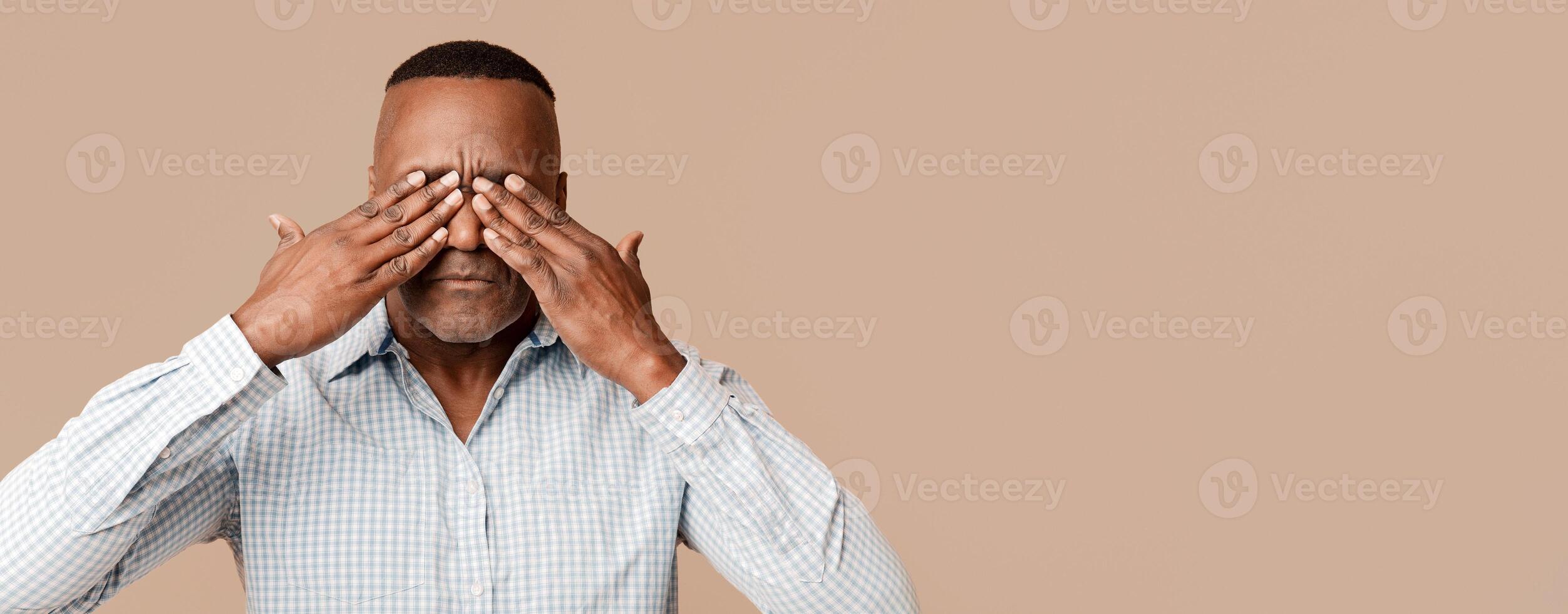 See no evil. Mature african man closing his eyes, orange studio background photo