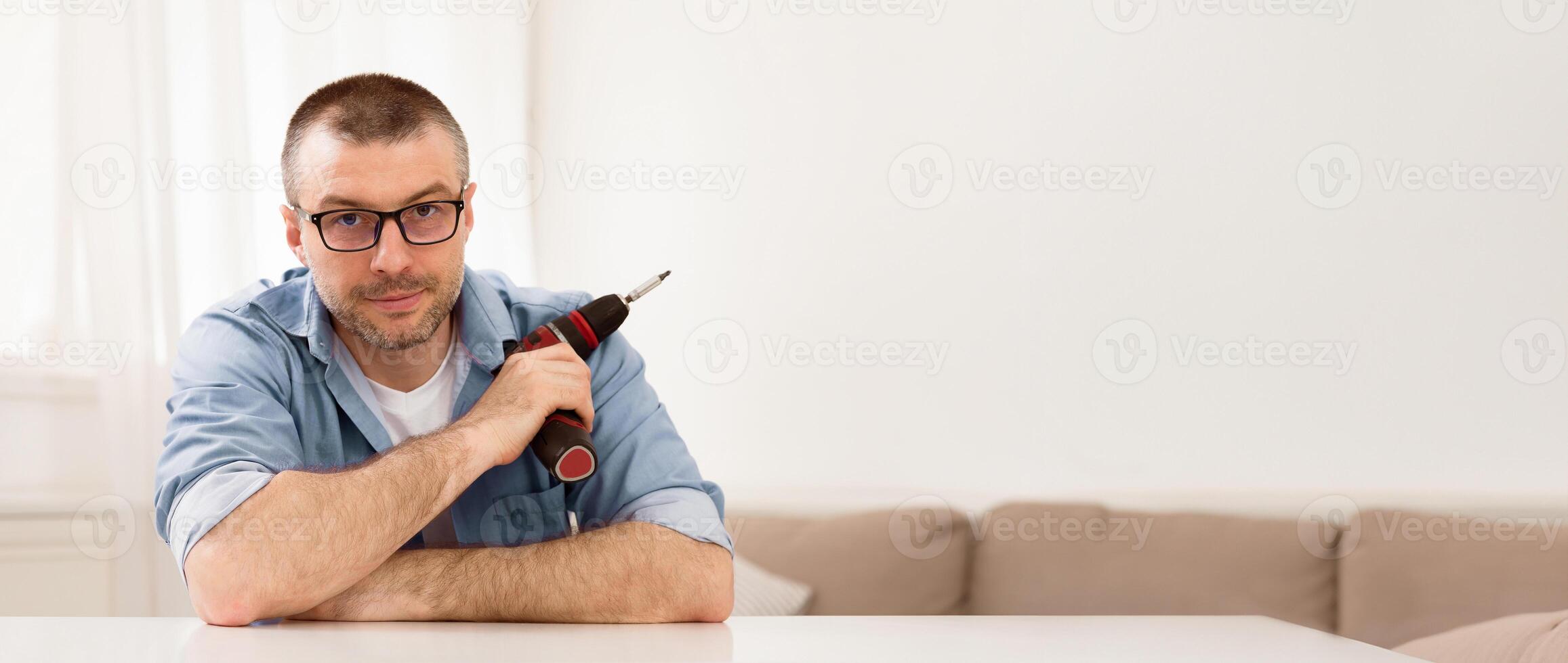 Furniture Assembly. Man Holding Electric Drill Fixing Table Using Carpentry Tools Sitting Looking At Camera At Home. photo