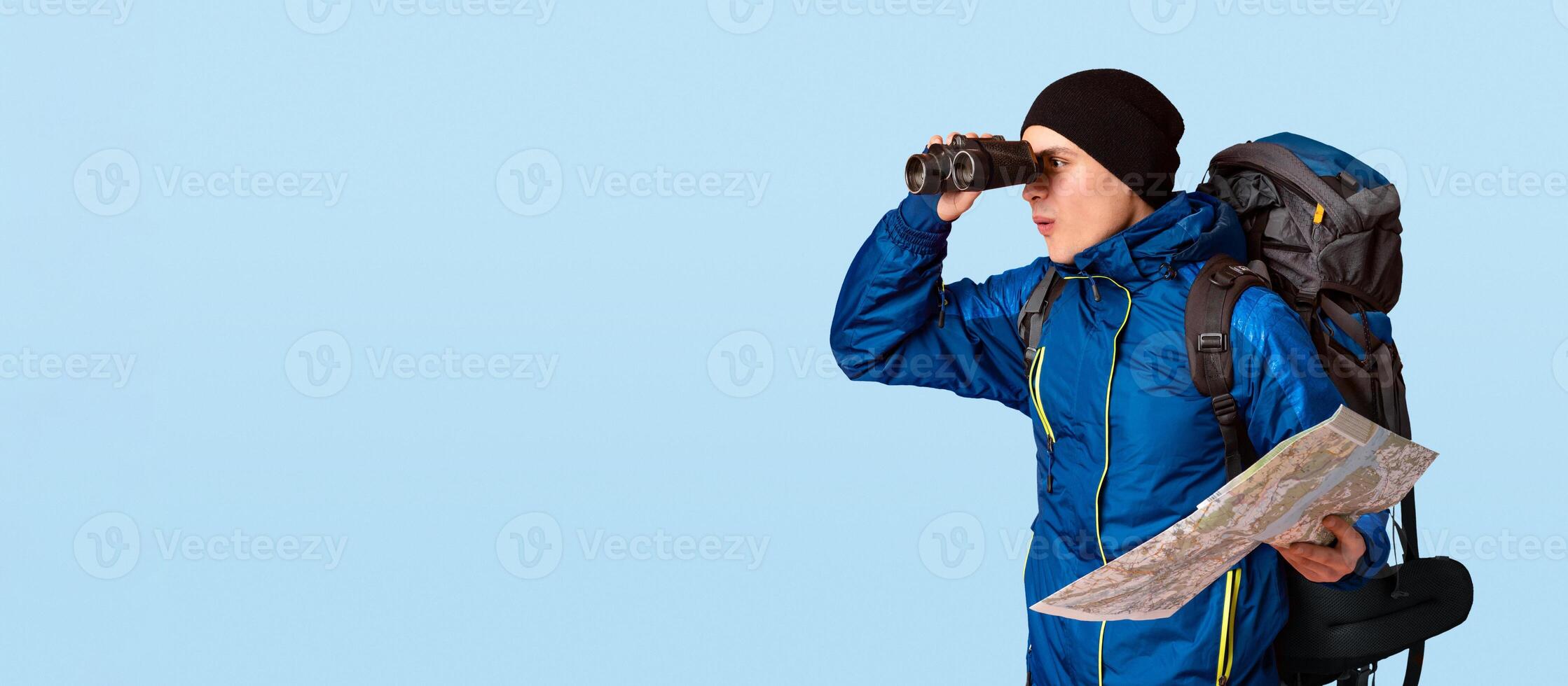 Hiker with map through binoculars at free space, orange studio background, panorama photo