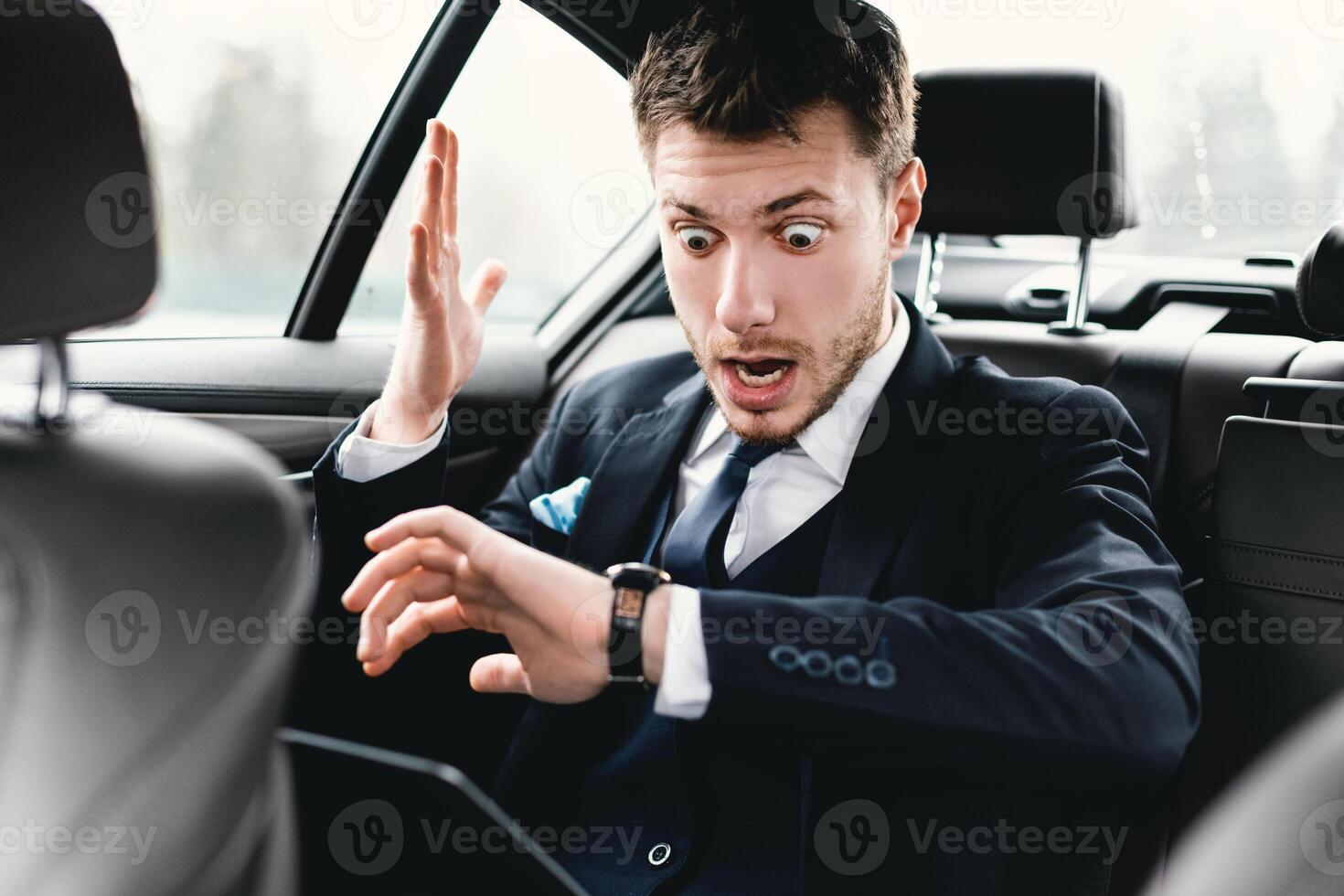 Late For Meeting, Work Or Flight. Shocked businessman sitting on backseat of car and checking time on wrist watch photo