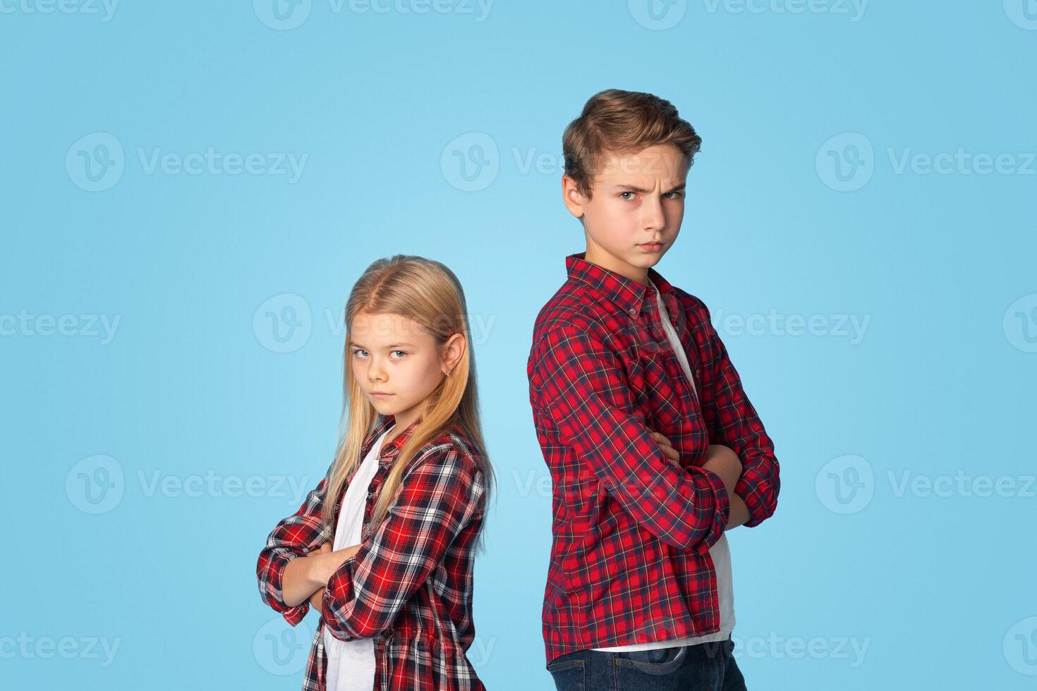 Siblings Conflicts. Offended Brother And Sister Standing Back To Back Not Talking To Each Other After Quarrel, Blue Studio Background With Copy Space photo