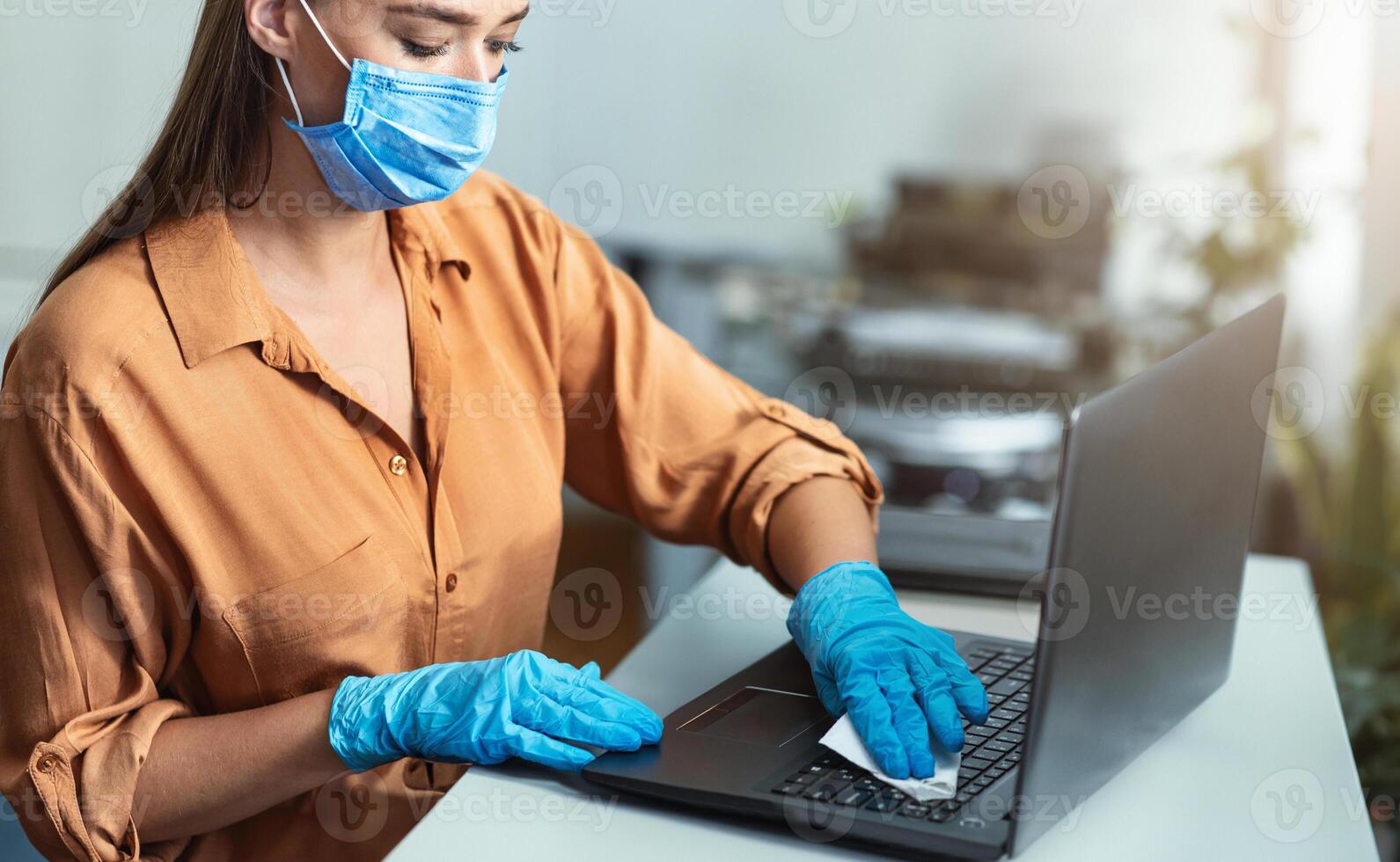 Antiseptic Treatment Concept. Girl in mask and gloves cleaning laptop keyboard with disinfectant photo