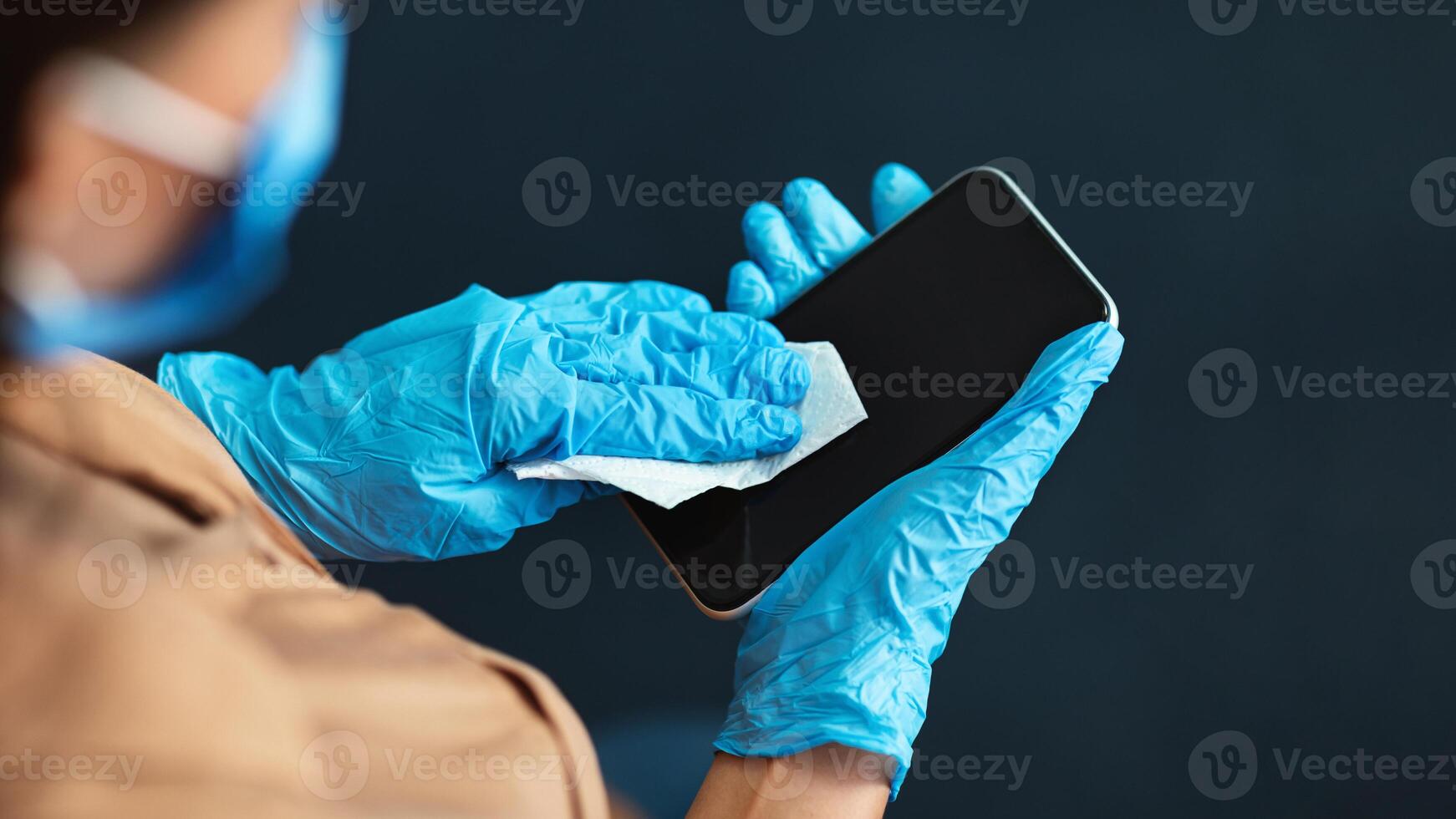 Coronavirus outbreak contamination prevention concept. Woman wearing gloves cleaning mobile phone with disinfectant. Copy space photo