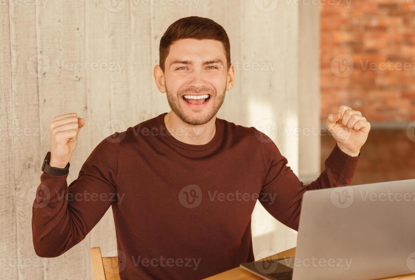 Business Success. Happy Man Shaking Fists Sitting At Laptop Celebrating Promotion In Modern Office. Selective Focus photo