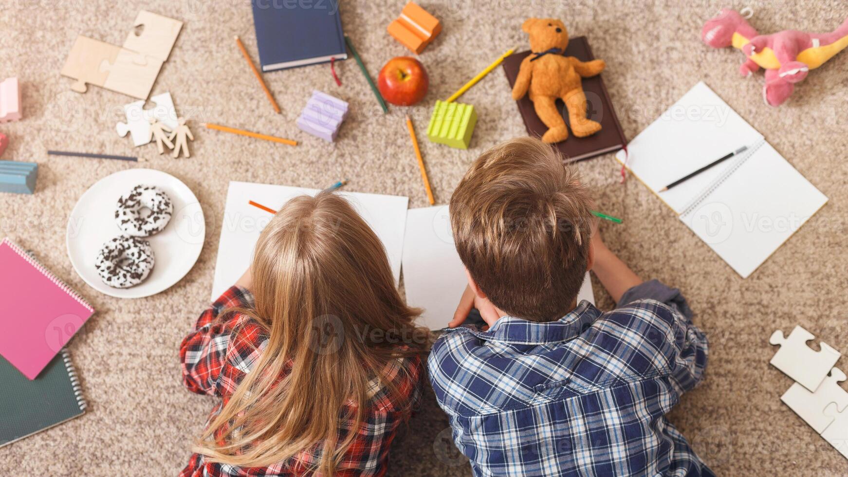 Unrecognizable Brother And Sister Drawing Doing Homework Together Lying On Floor Indoor. Above View photo