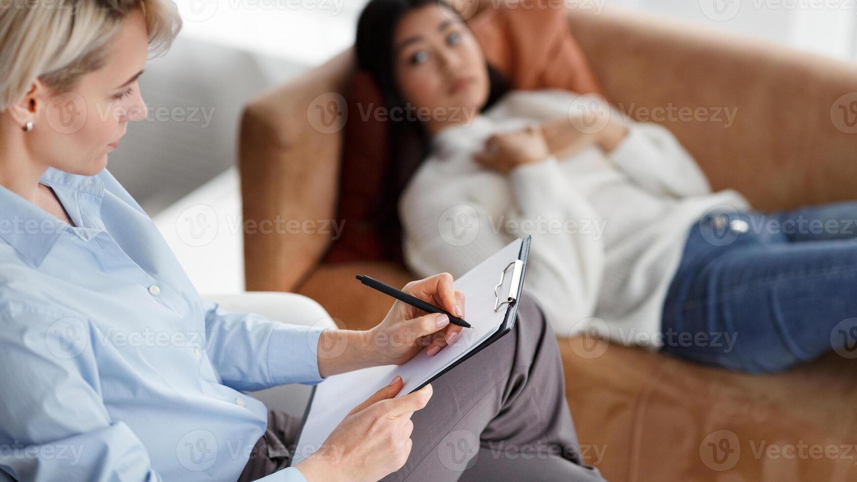 Professional Psychologist Taking Notes Listening To Depressed Female Patient Lying On Couch In Office. Selective Focus photo
