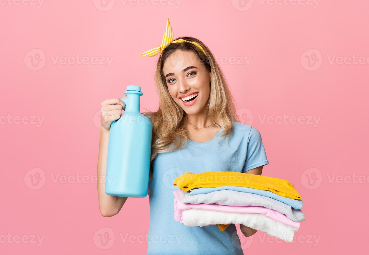Washing concept. Smiling young blonde holds in hands folded clean fresh stuff and bottle of cleaning supply photo
