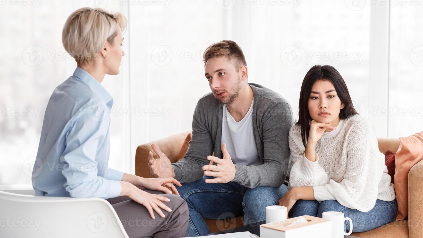 Couple At Family Therapy Session. Unhappy Spouses Talking With Counselor Discussing Family Problems And Quarrels Sitting In Office. Selective Focus photo