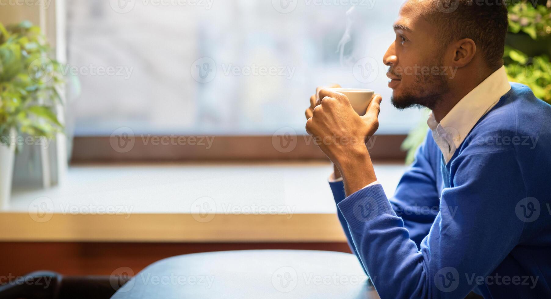 Good Start Of The Day. Pensive black guy holding white mug at cafe, drinking coffee at breakfast and thinking photo