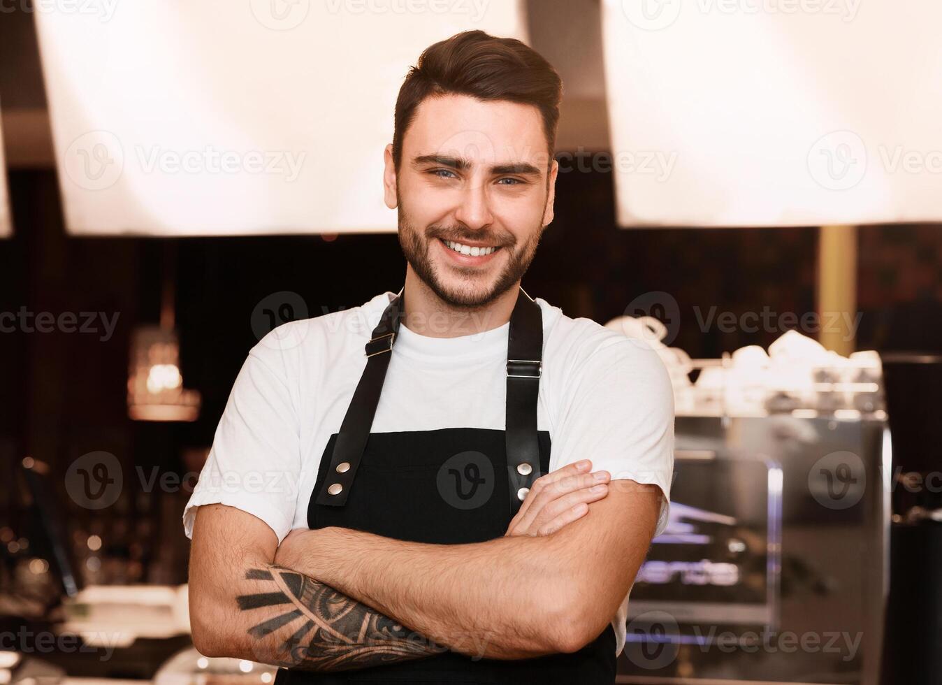 Professional Barista. Smiling Barkeeper Guy In Uniform Standing Near Counter With Coffee-Machine In Coffee Shop photo