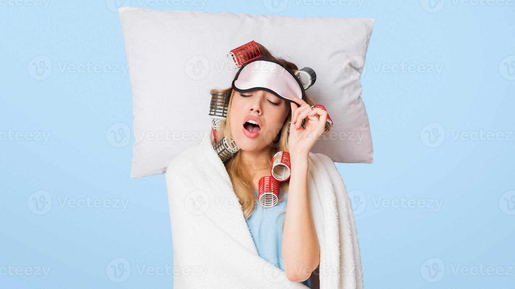 Sleeping beauty with curlers on head wakes up, yawns and removes sleeping mask photo