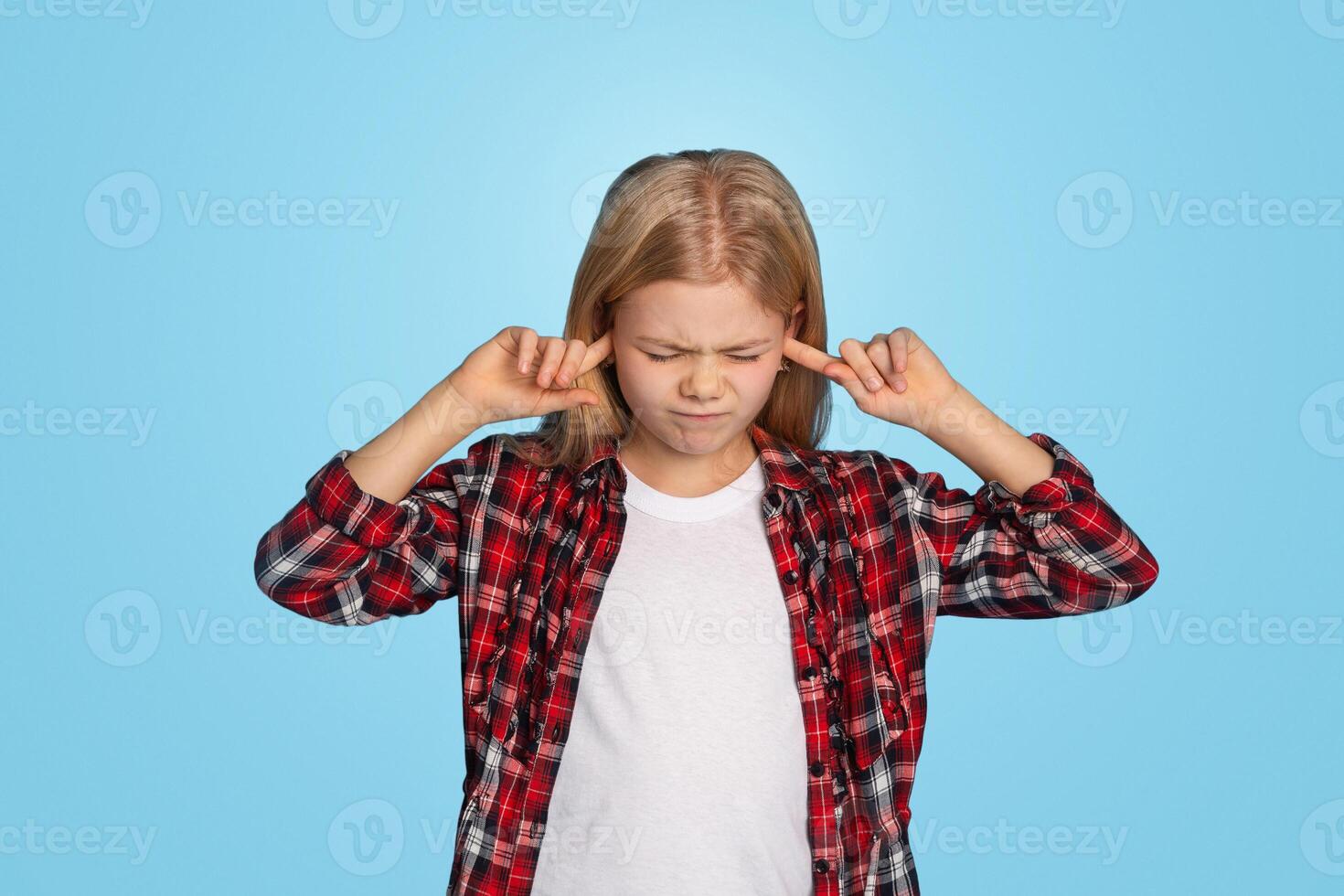 Naughty little girl closing ears with fingers, doesn't want to hear something, standing over blue studio background, panorama with empty space photo