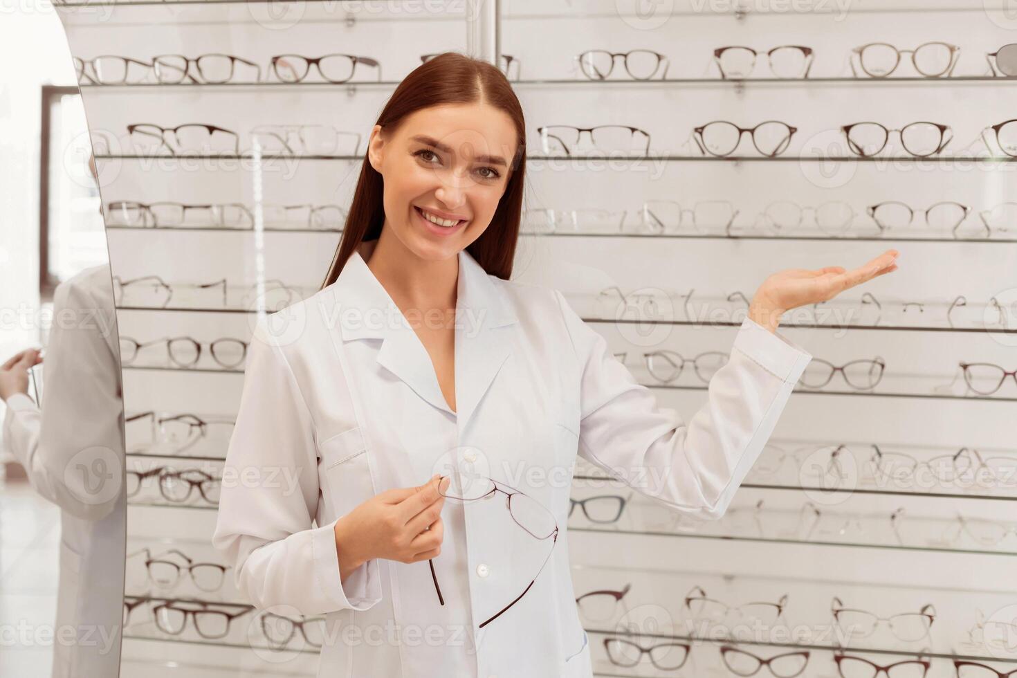 Beautiful lady ophthalmologist seller showing range of eyeglasses frame in optical store photo