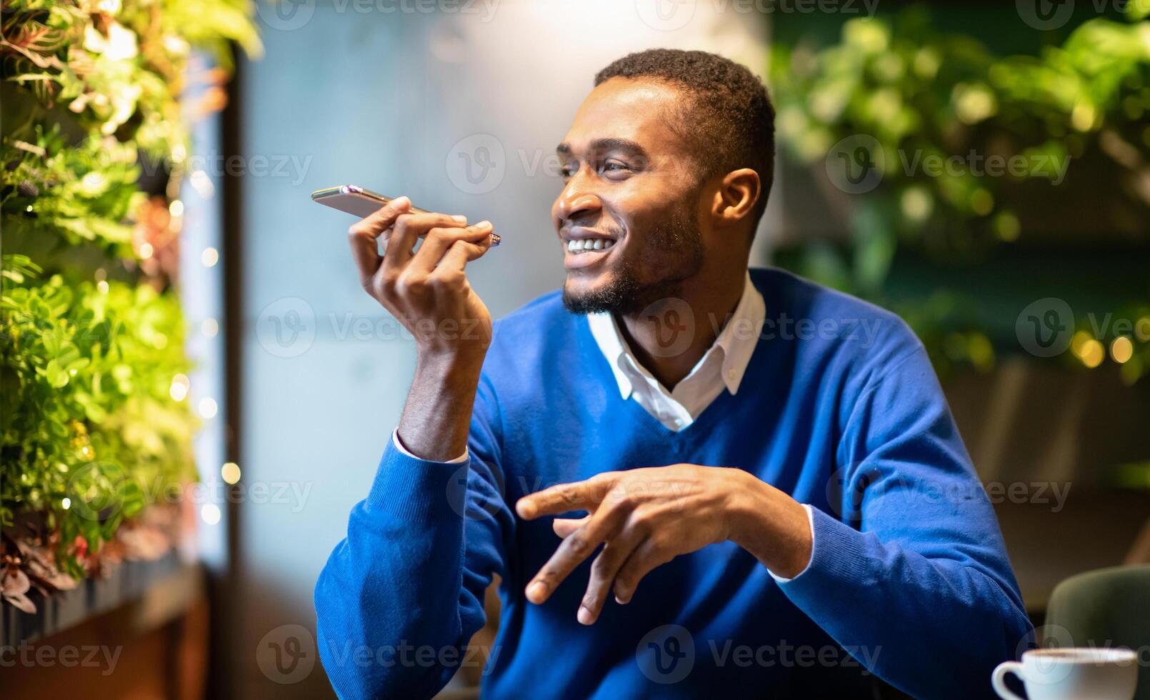 Voice Search. Happy black man using voice assistant on mobile phone or calling on smartphone at cafe, copyspace photo