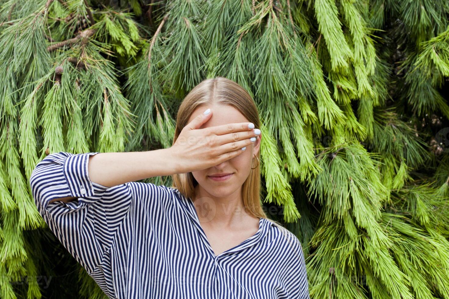 Woman wearing elegant clothes hiding her face standing in the forest against fir trees. photo
