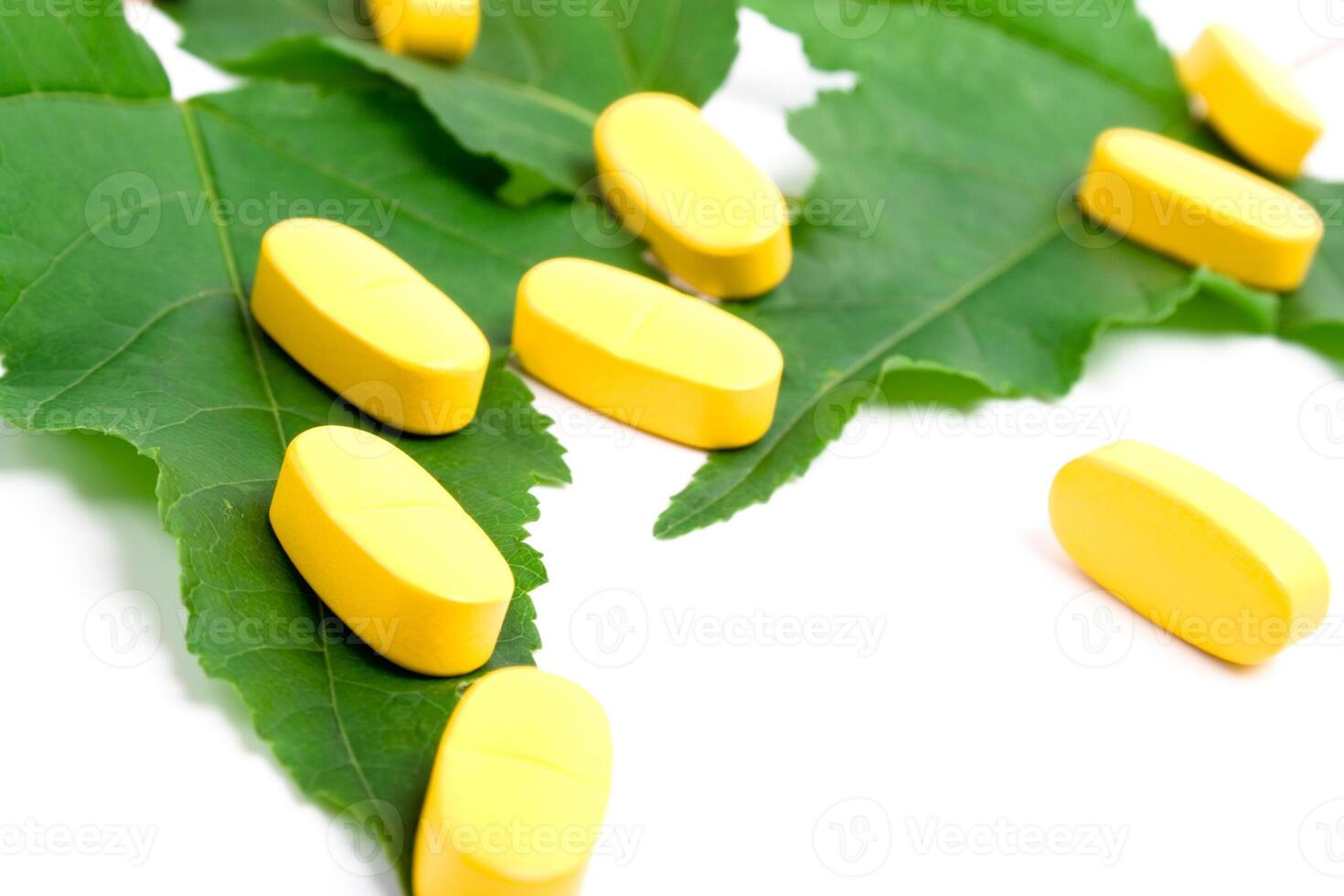 yellow vitamin pills over green leaves photo
